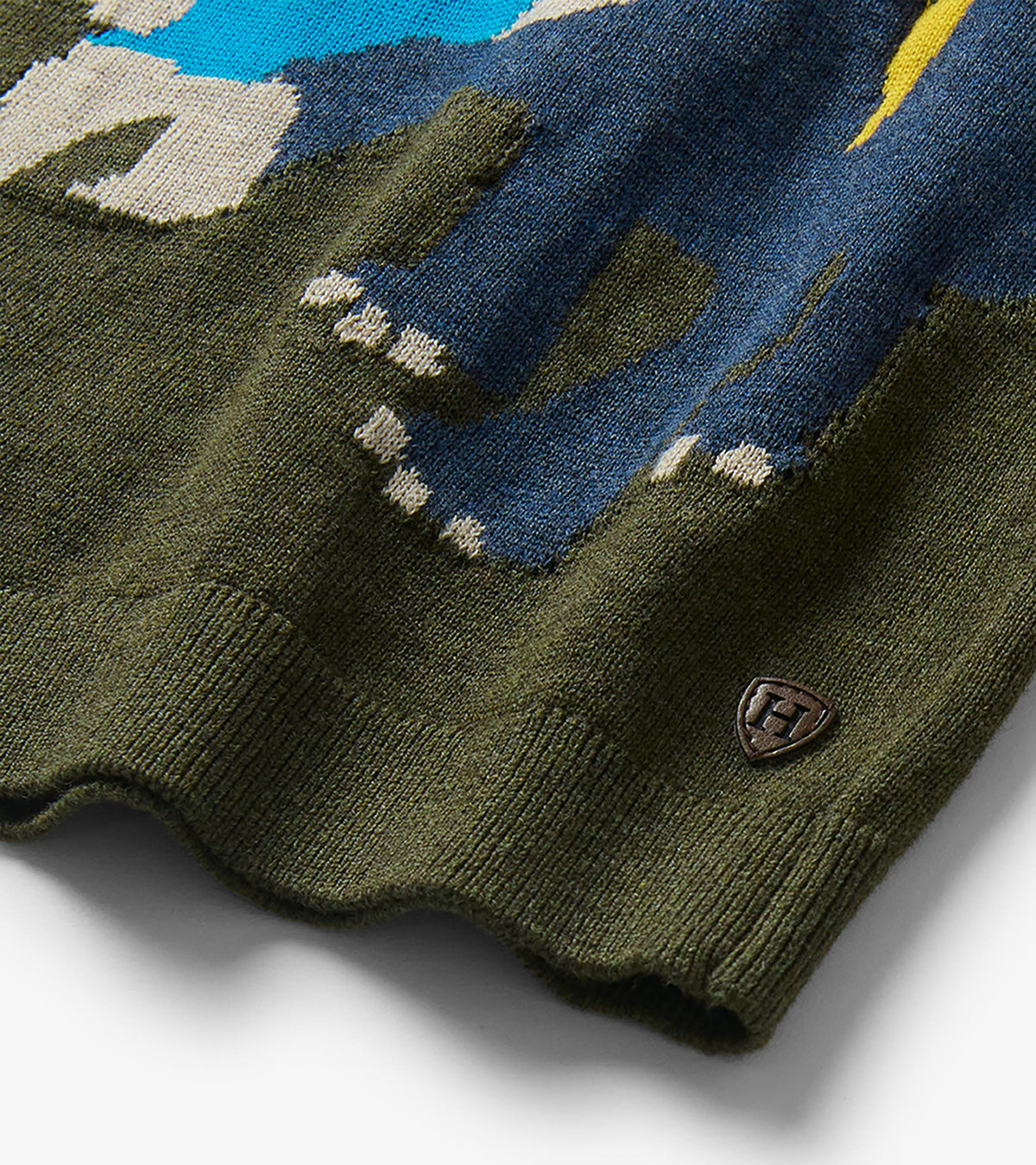 Close-up of the sweater hem and triceratops knit detail in blue, yellow, gray, and olive green