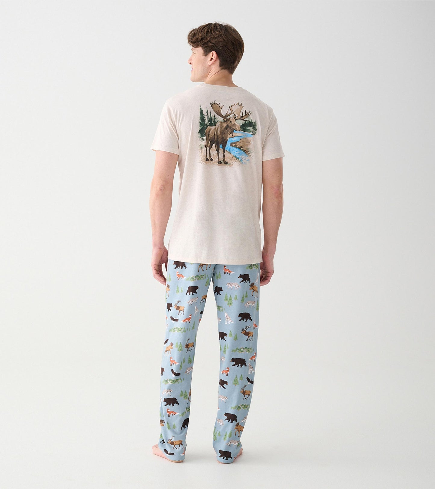 Back view of model wearing light blue wilderness print pajama pants and beige T-shirt with moose graphic