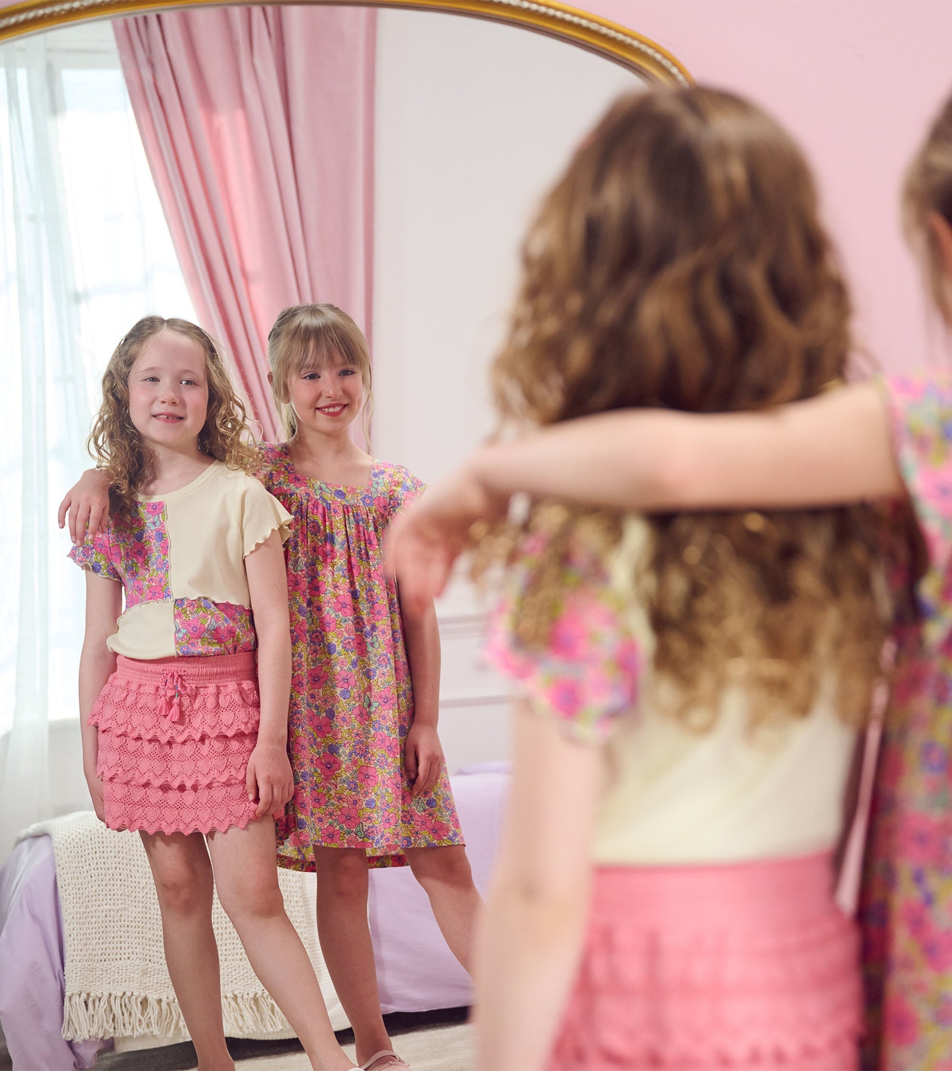 Pink skort with heart pattern and layered ruffles, styled with a floral top, worn by two girls in a mirror reflection.