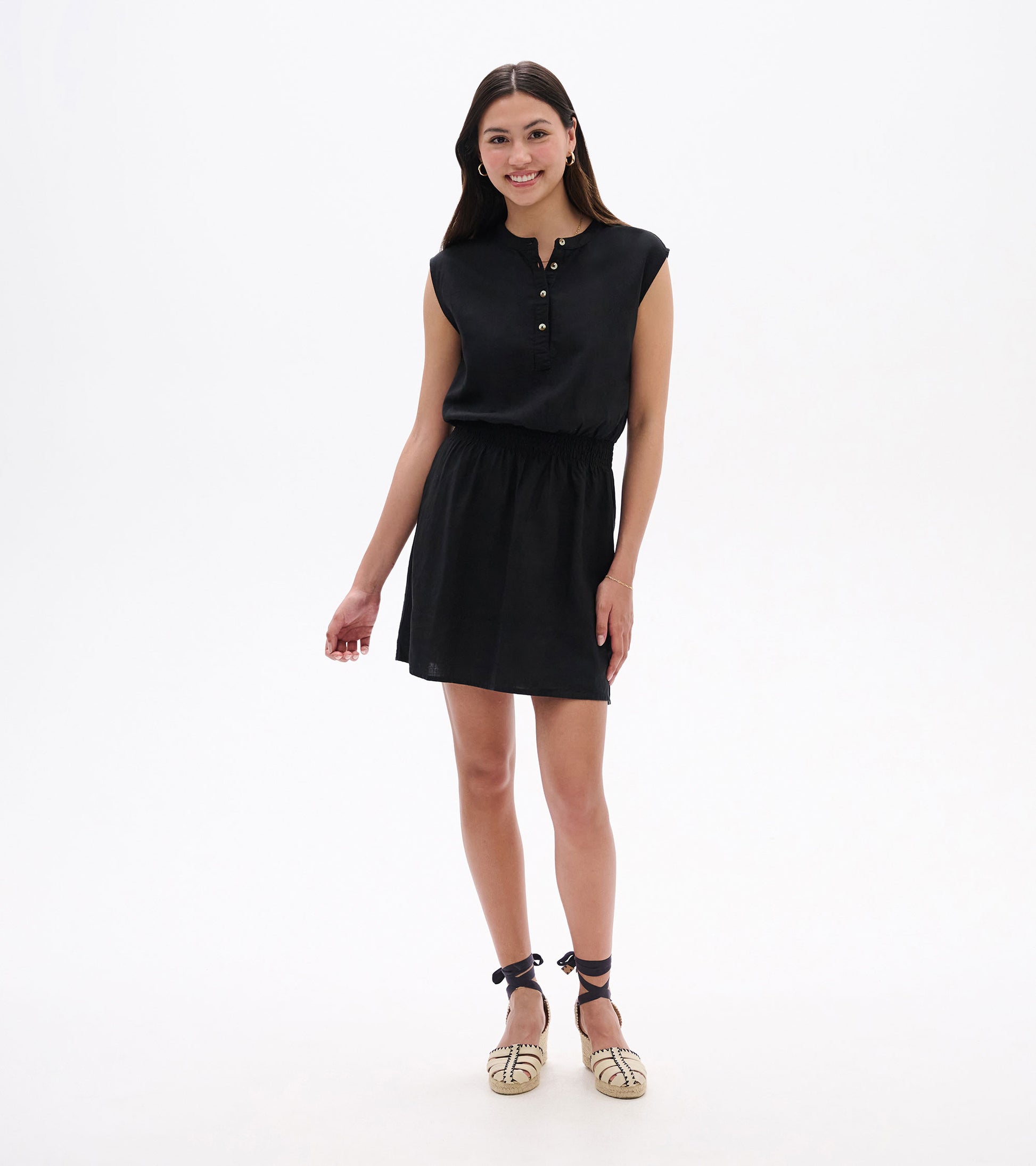 Black sleeveless dress with a buttoned neckline and elastic waist, styled with espadrille sandals.