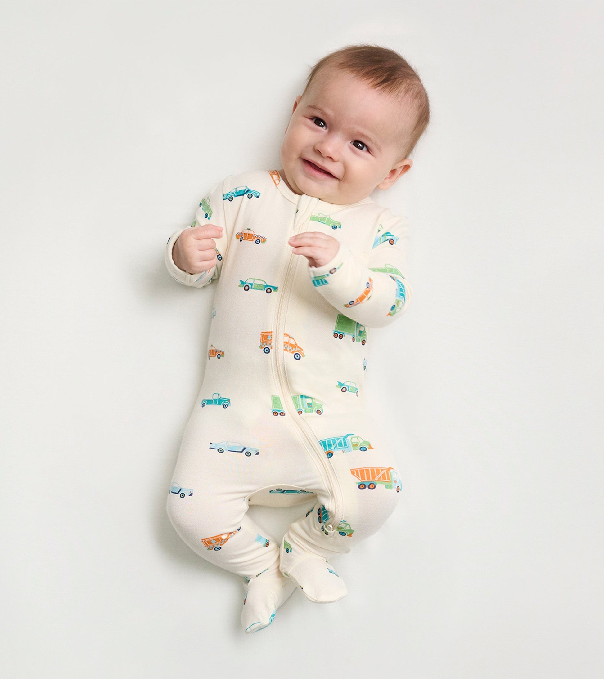 Cream footed sleeper for baby boys featuring colorful car and truck prints, with a front zipper and snug fit.