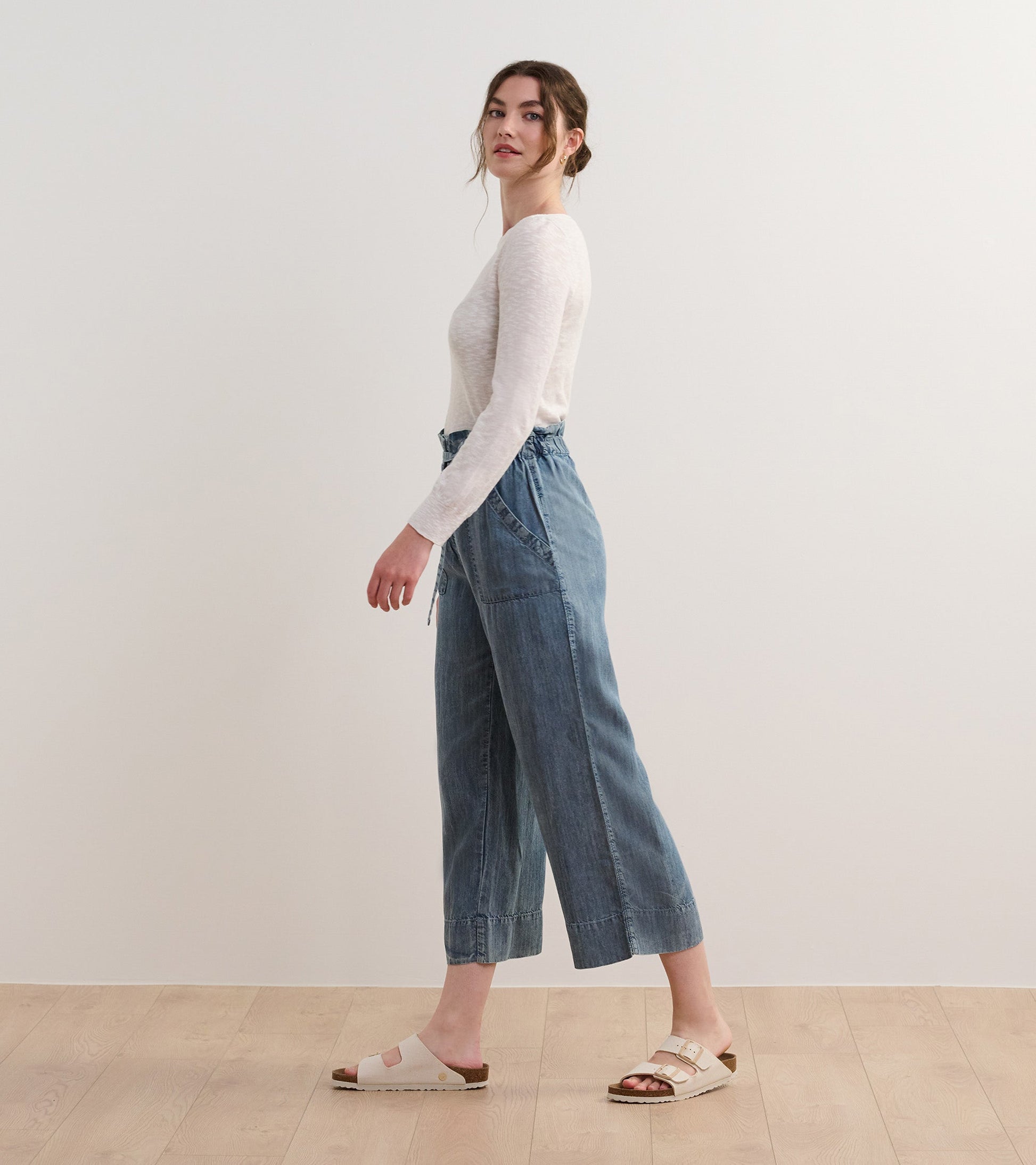 White 3/4 sleeve knit top paired with denim culottes and sandals, shown from the side.