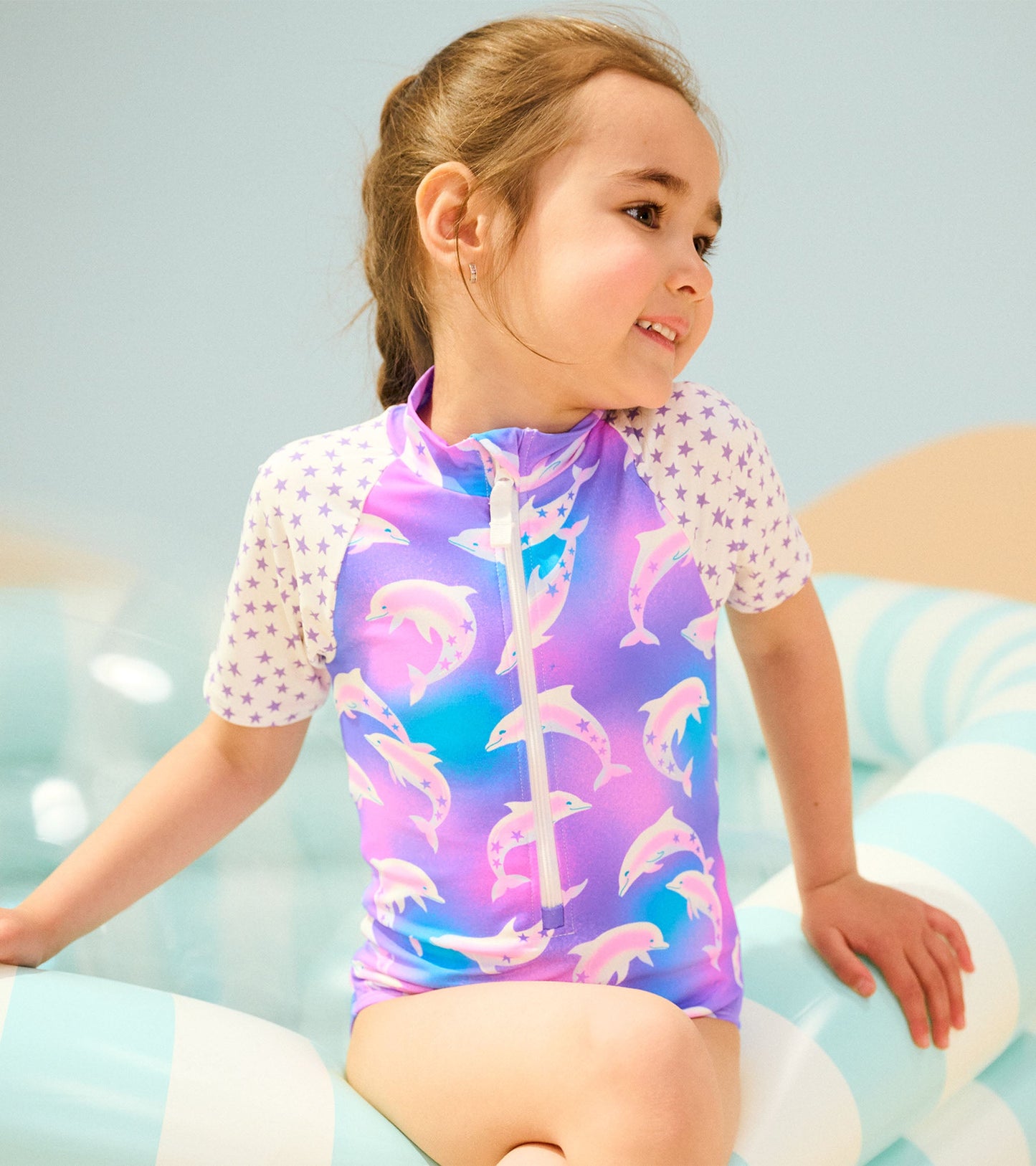 Purple one-piece rashguard featuring dolphin prints and star-patterned sleeves, ideal for swimming and sun protection.
