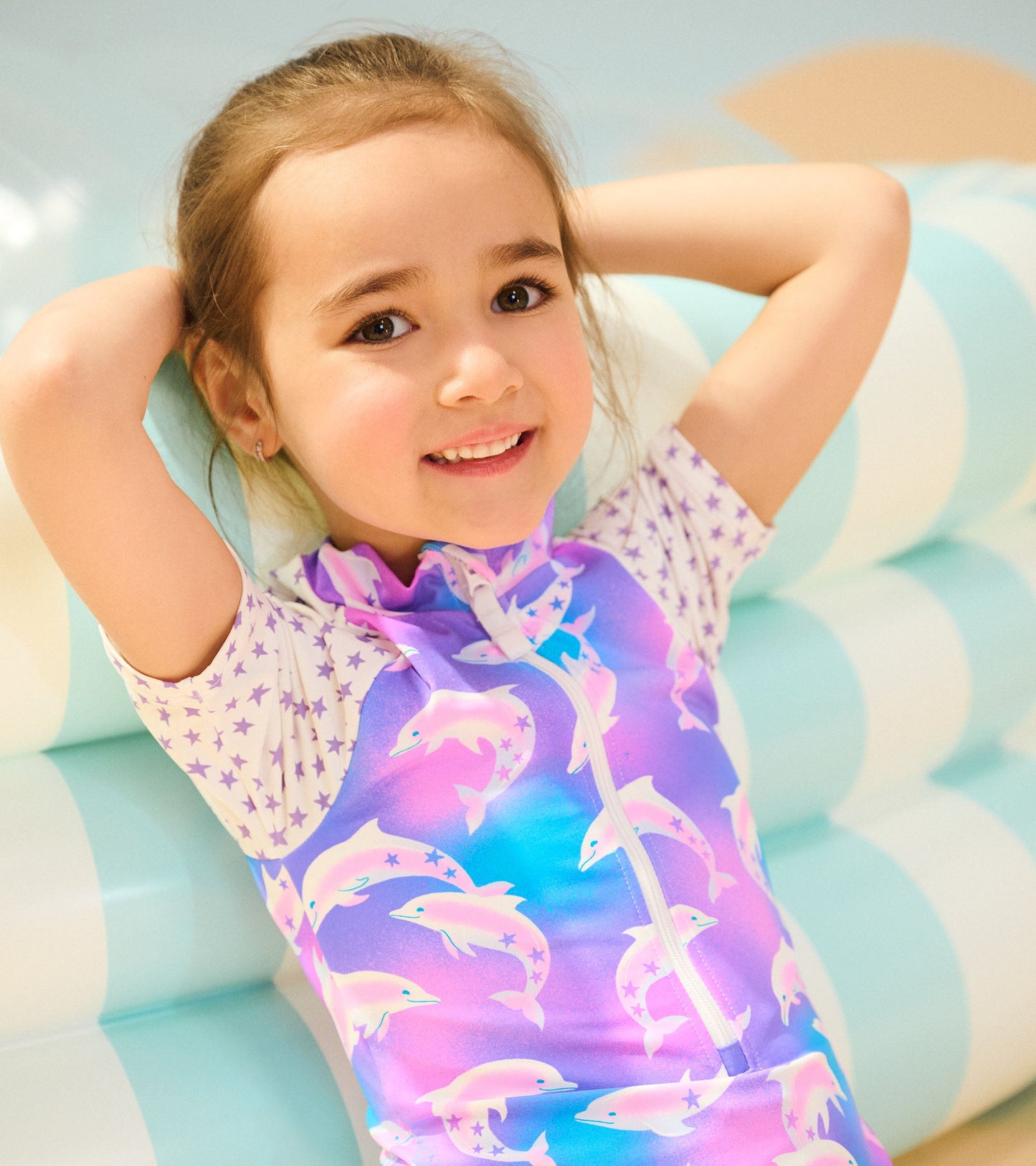 Colorful one-piece rashguard featuring dolphins and stars, with a zip front and short sleeves, suitable for water activities.