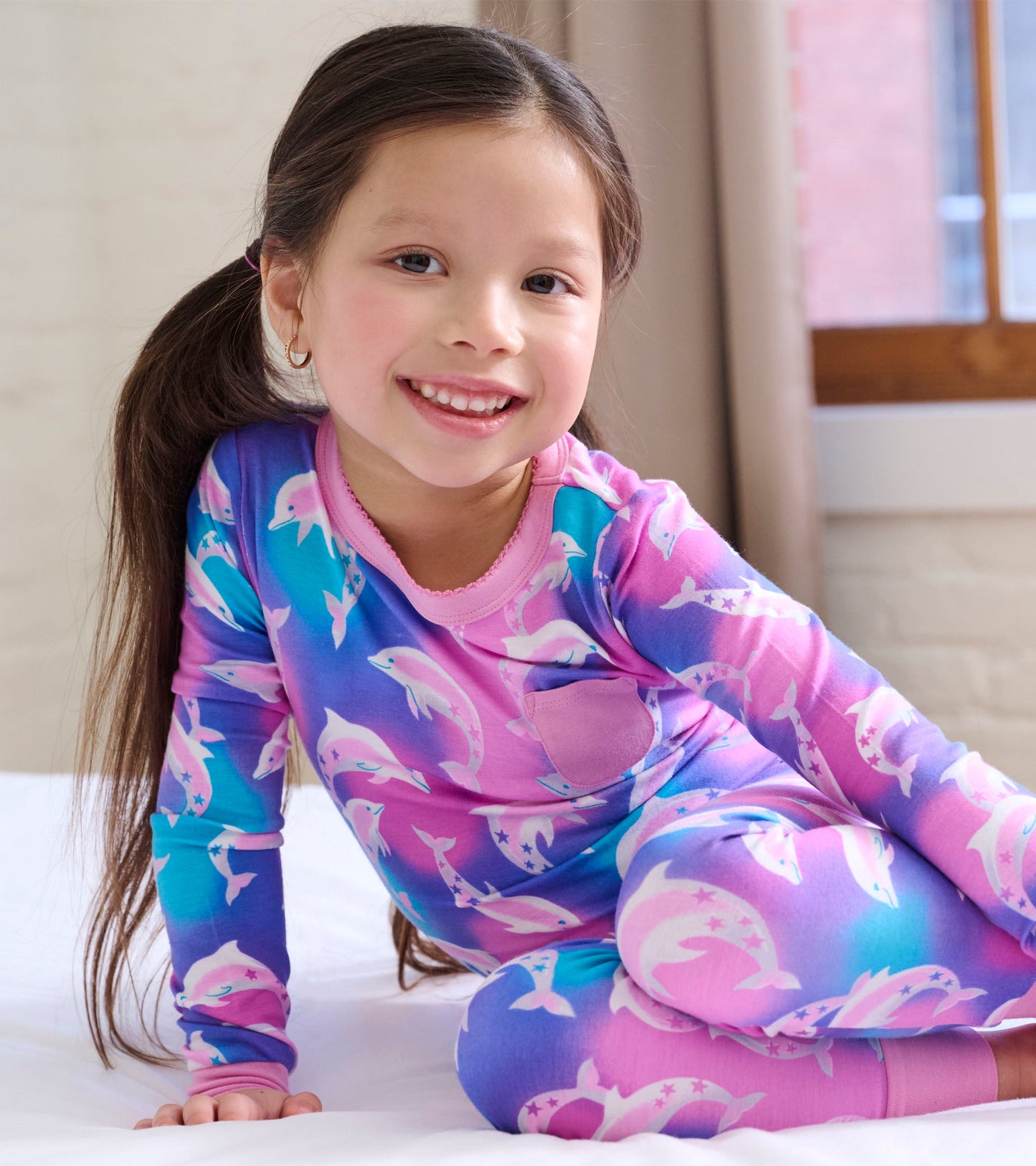 Girls' long-sleeve pajama set featuring colorful dolphins on a pink and blue gradient background.