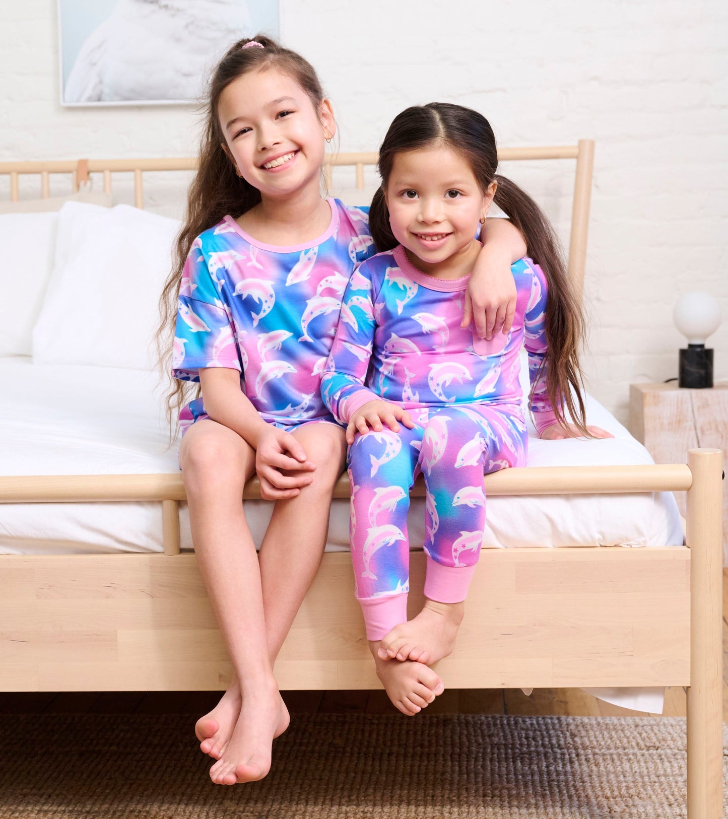 Girls' bamboo pajama set featuring a colorful dolphin pattern, short sleeves, and long pants, worn by two smiling children.