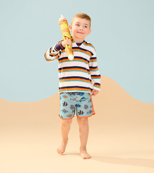 Striped terry pullover hoodie in white, blue, and orange, worn by a boy with fish-patterned shorts, holding a beach umbrella.