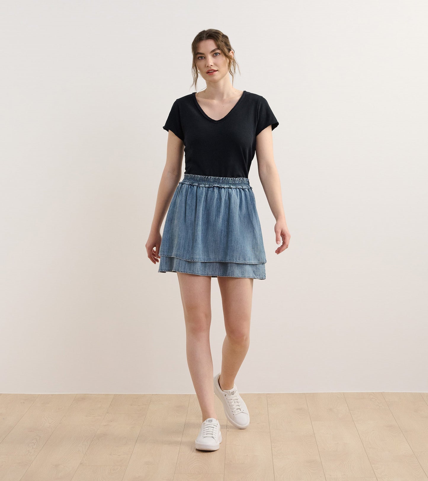 Blue acid wash layered smocked skirt with an elastic waistband, styled with a black top and white sneakers.