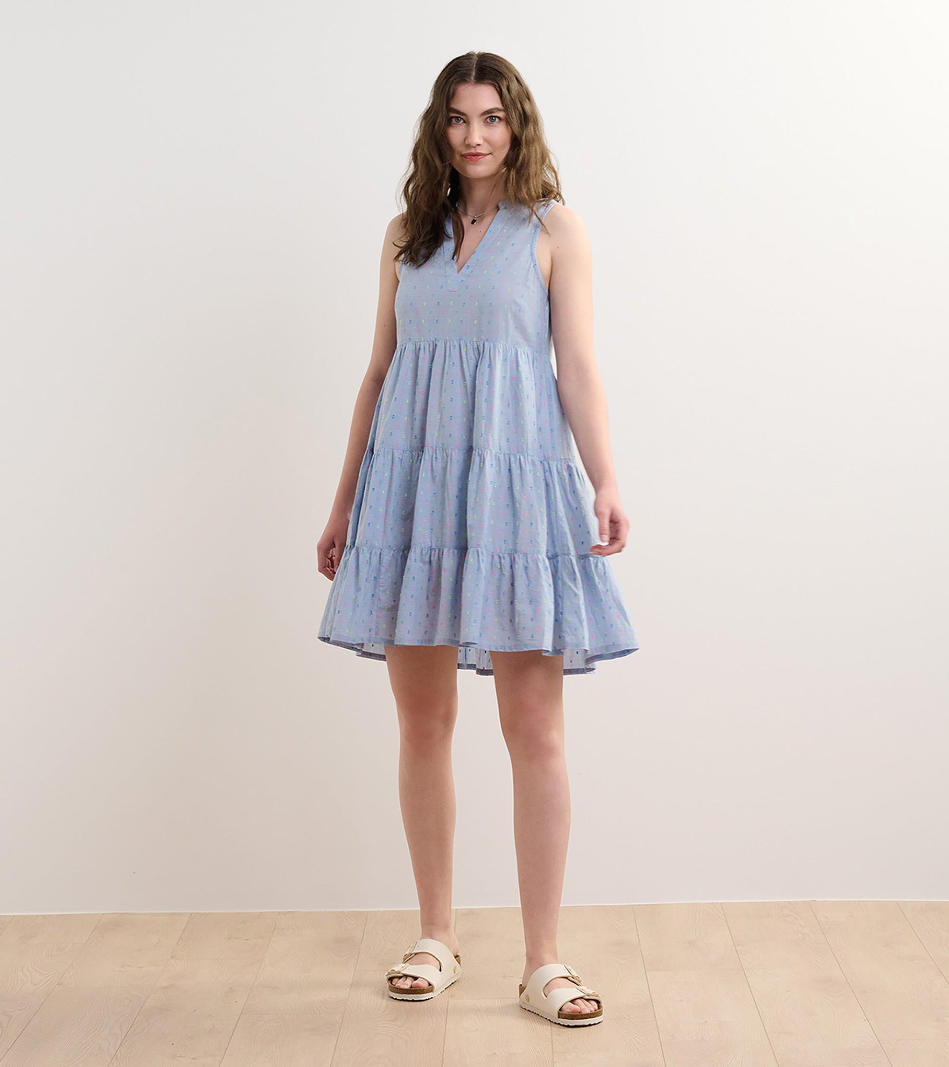 Light blue chambray dress with a tiered design and colorful spots, featuring a V-neck and sleeveless style.