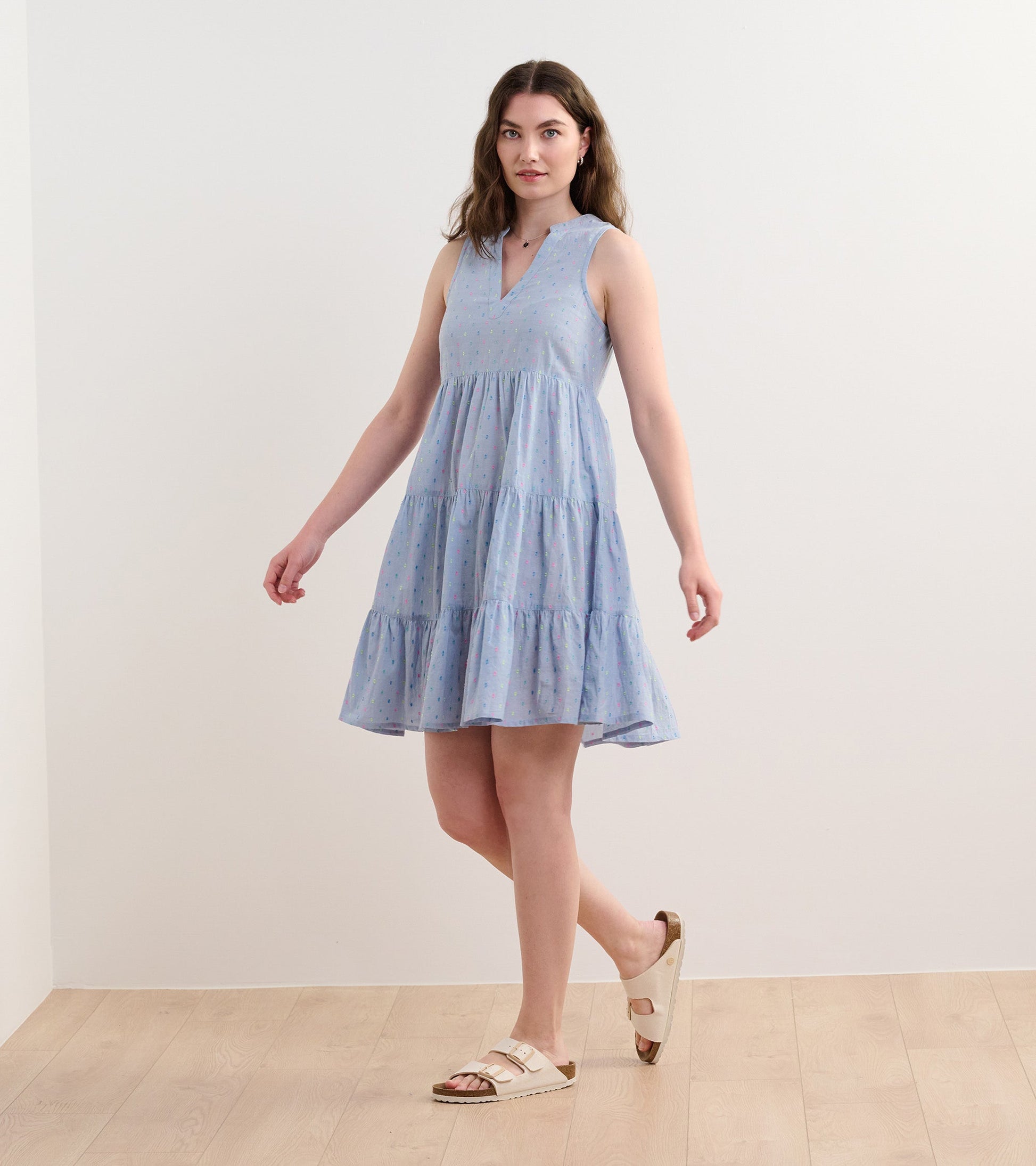 Light blue chambray dress with a tiered design and colorful spots, featuring a v-neck and sleeveless style.