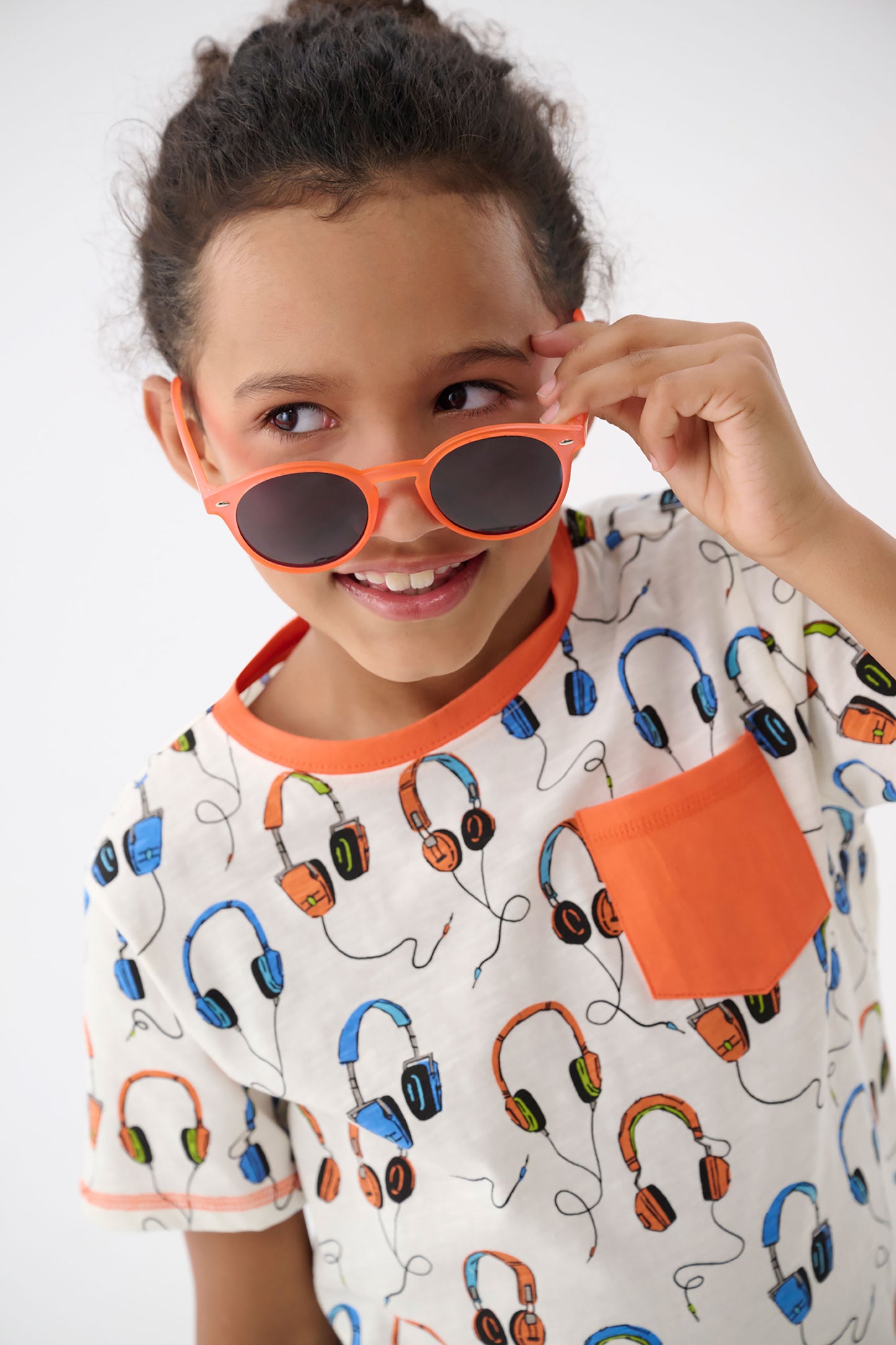 White t-shirt featuring colorful headphone prints and an orange pocket, suitable for boys.