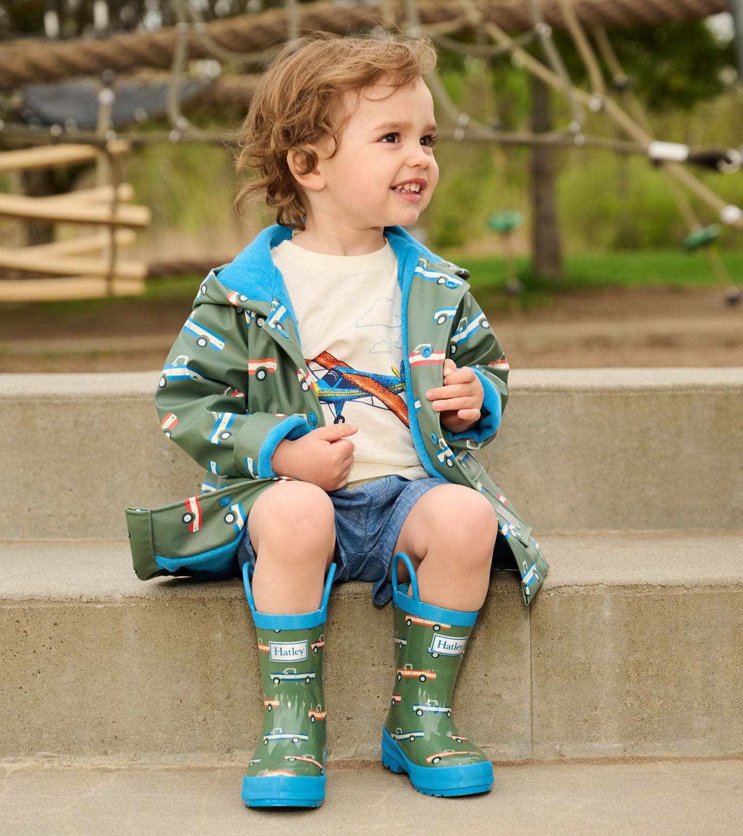 Green rain boots with blue handles, featuring a colorful truck pattern, perfect for toddlers.
