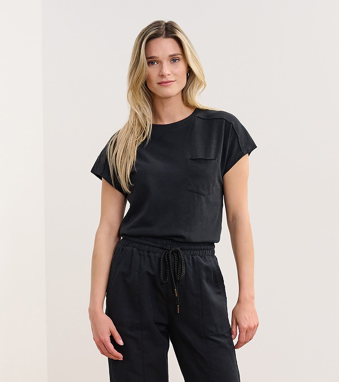 Black slouchy tee with short sleeves and a chest pocket, styled with relaxed-fit pants.