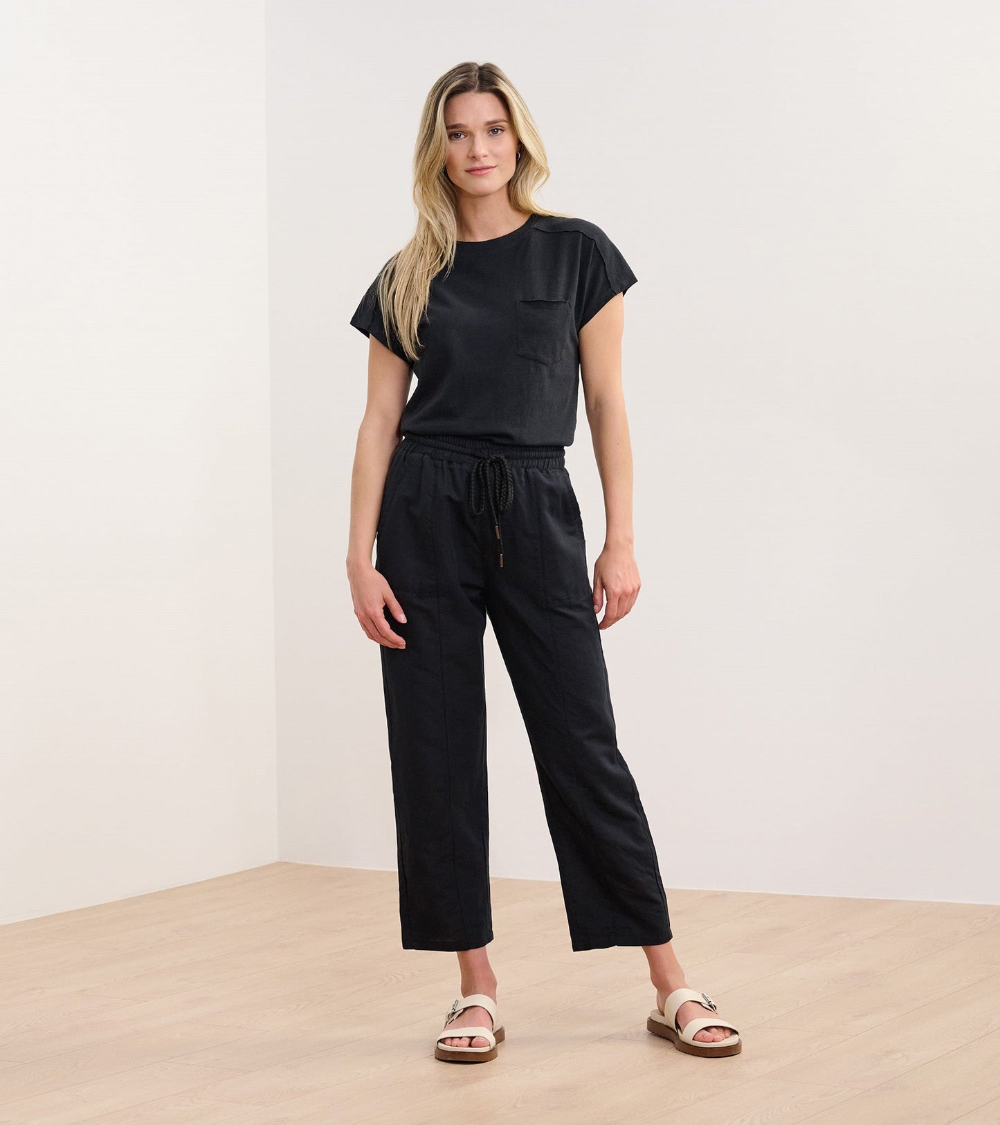 Black slouchy pocket tee with short sleeves, paired with matching black pants, worn by a model standing on a wooden floor.