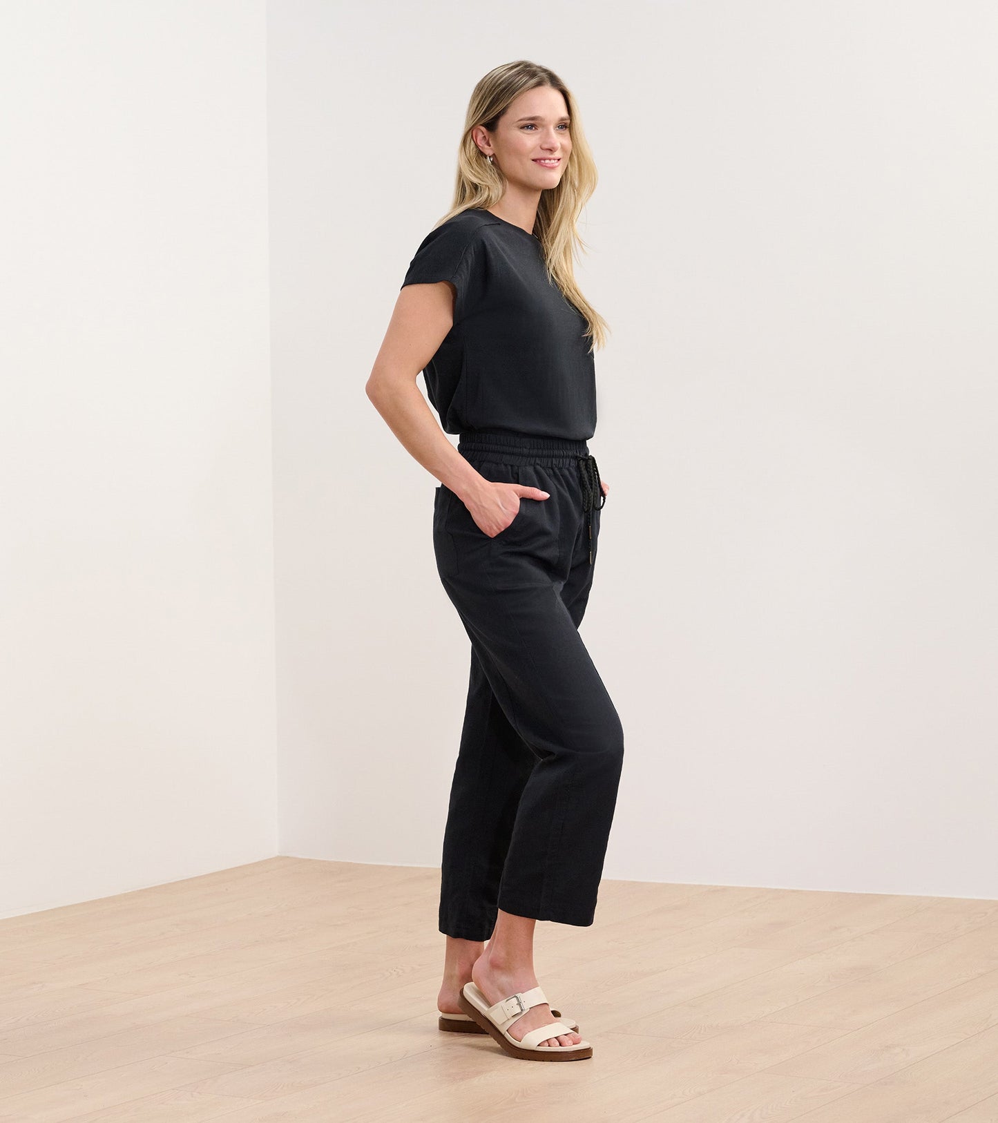 Black slouchy pocket tee with short sleeves, styled with relaxed black pants and sandals, shown from the side.