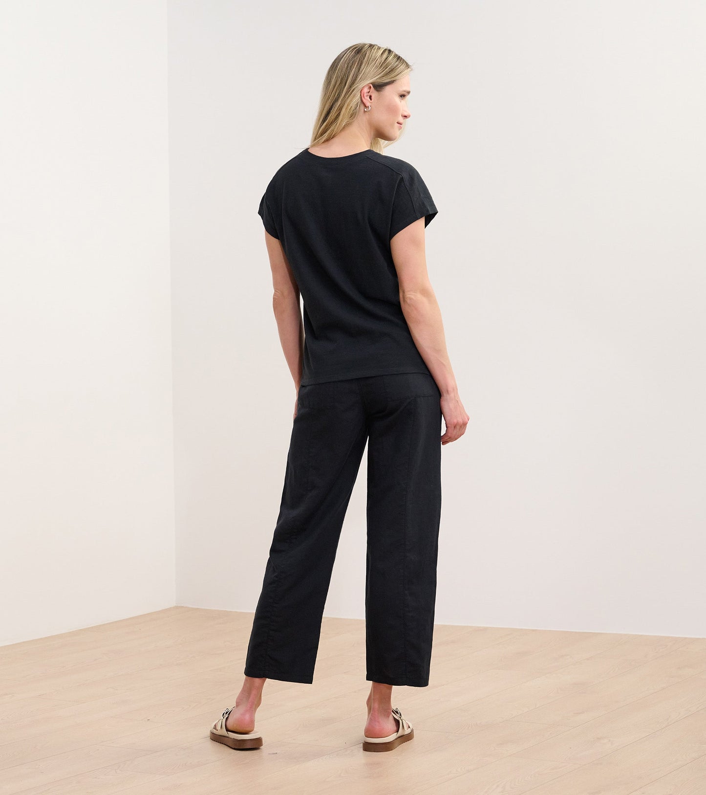 Black slouchy pocket tee with short sleeves, shown from the back, paired with black pants and sandals.