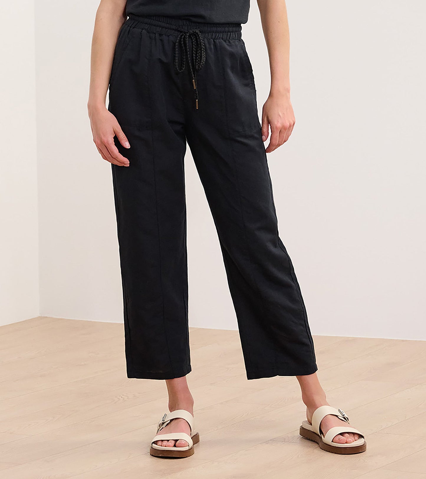 Black straight leg linen pants with an elastic waistband and drawstring, styled with a casual top and sandals.