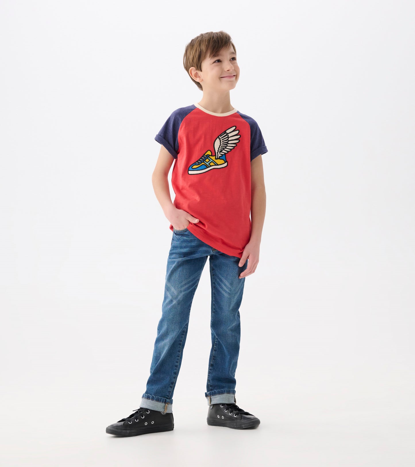 Red raglan t-shirt with blue sleeves and a winged sneaker graphic, worn by a boy with jeans and black shoes.