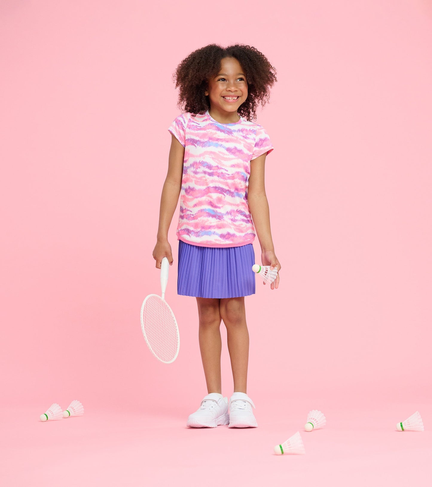 Pink and purple ombre mesh trim t-shirt worn by a girl, paired with a pleated purple skirt, holding a tennis racket.
