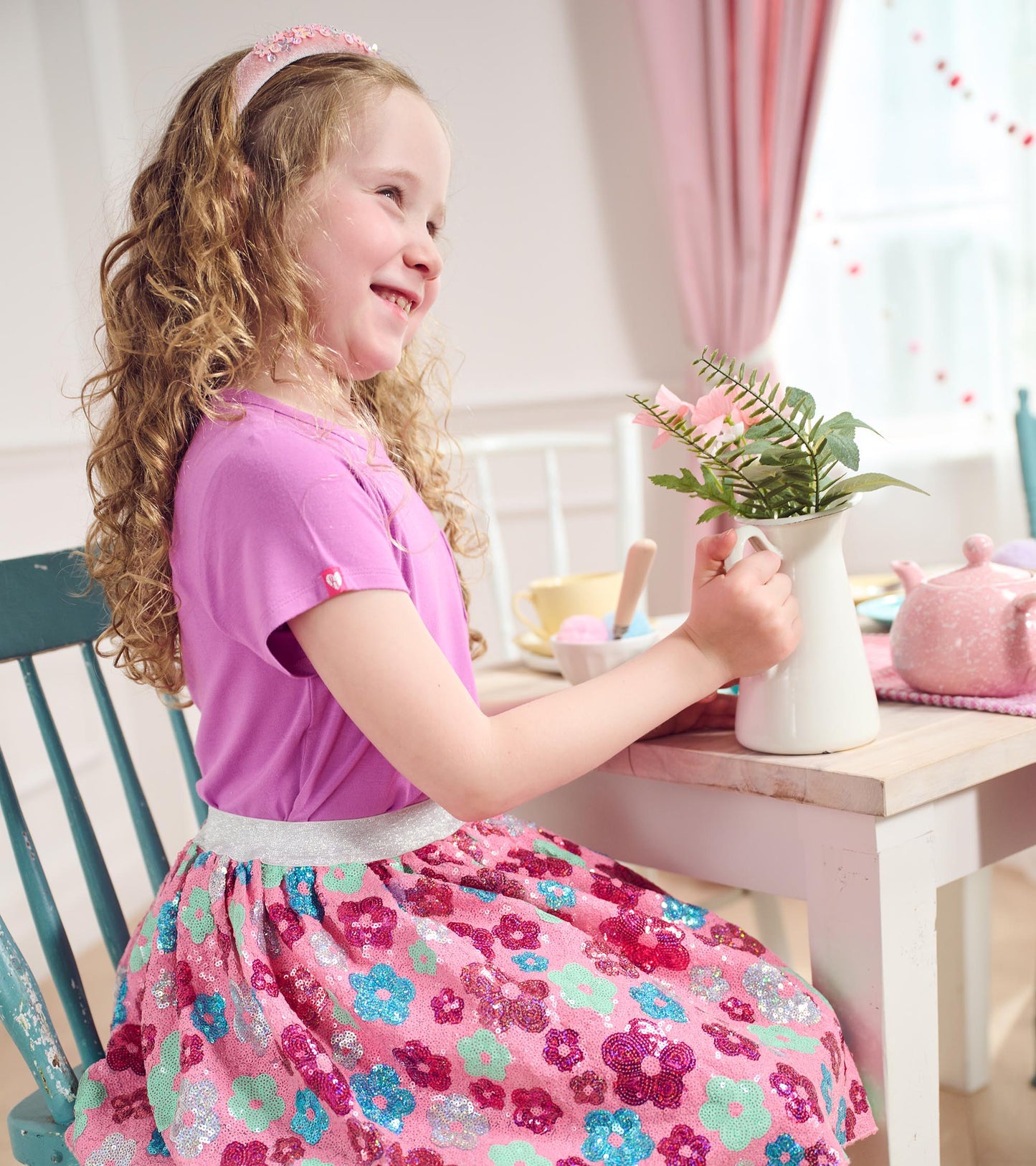 Pink tulle skirt with colorful daisy sequins, paired with a purple top, worn by a girl at a table with a vase.
