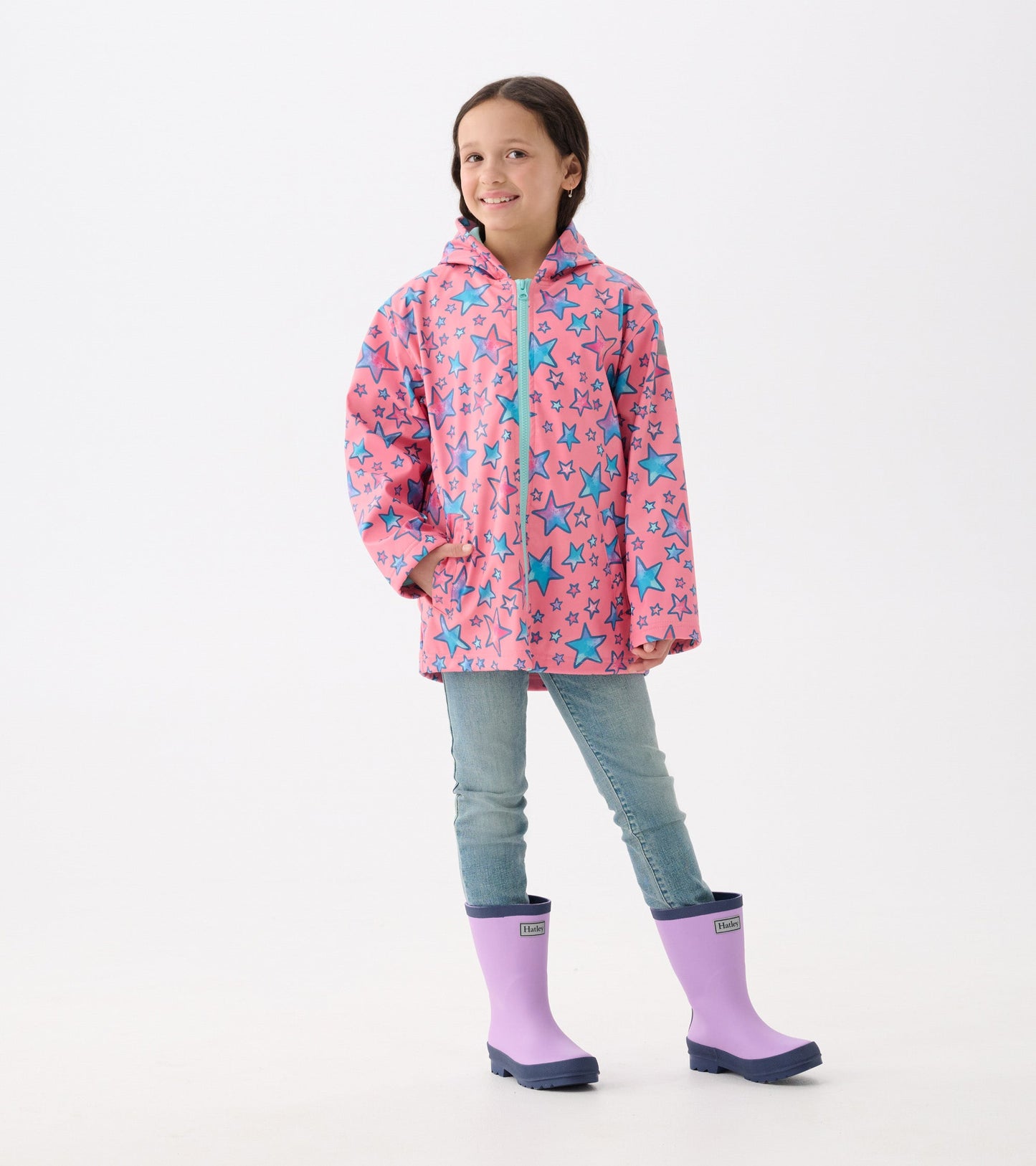 Pink zip-up rain jacket featuring blue star doodles, paired with light blue jeans and purple rain boots.