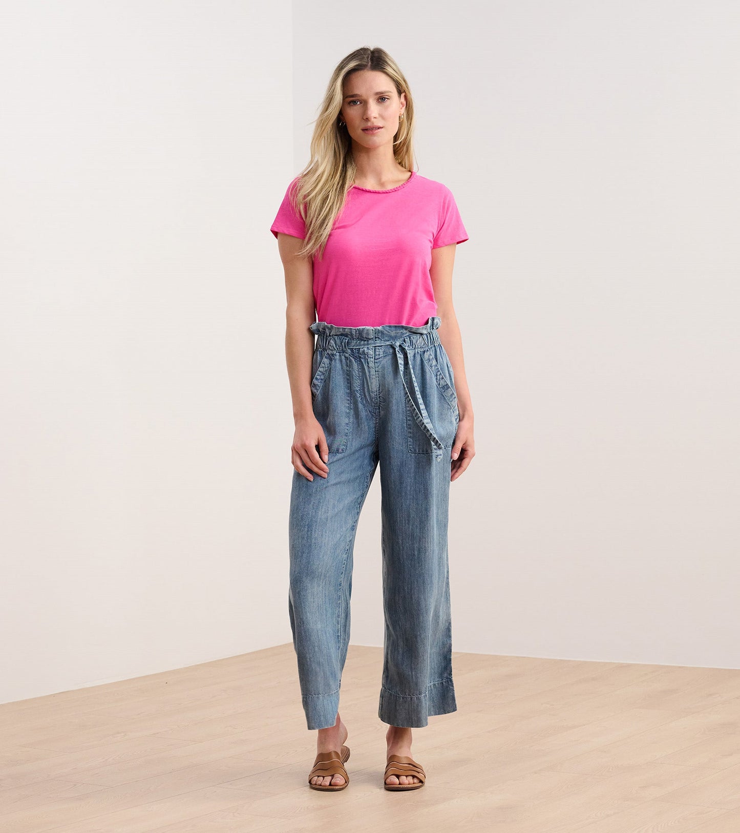 Fuschia braided neck tee paired with light blue wide-leg pants, model standing on a wooden floor.