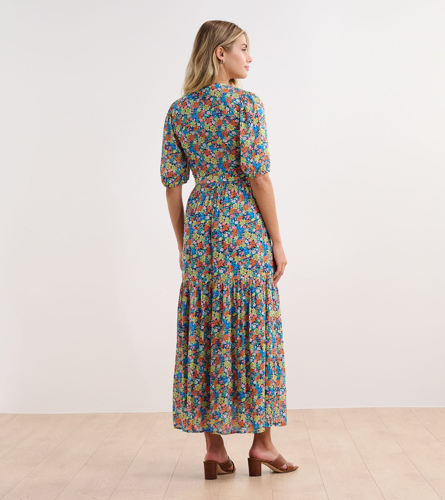 Floral maxi dress featuring a vibrant mix of colors, puff sleeves, and a tiered skirt, shown from the back.