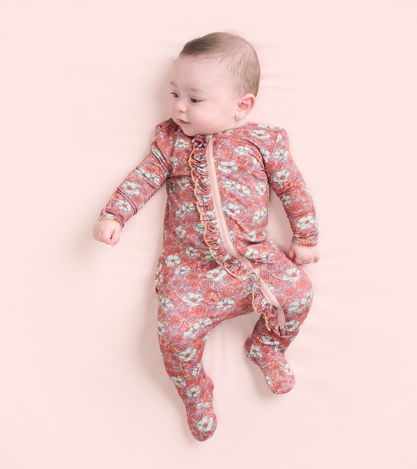 Footed sleeper for baby girls featuring a groovy floral pattern in pink and blue with ruffle details and a front zipper.