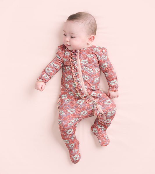Footed sleeper for baby girls featuring a groovy floral pattern in pink and blue with ruffle details and a front zipper.