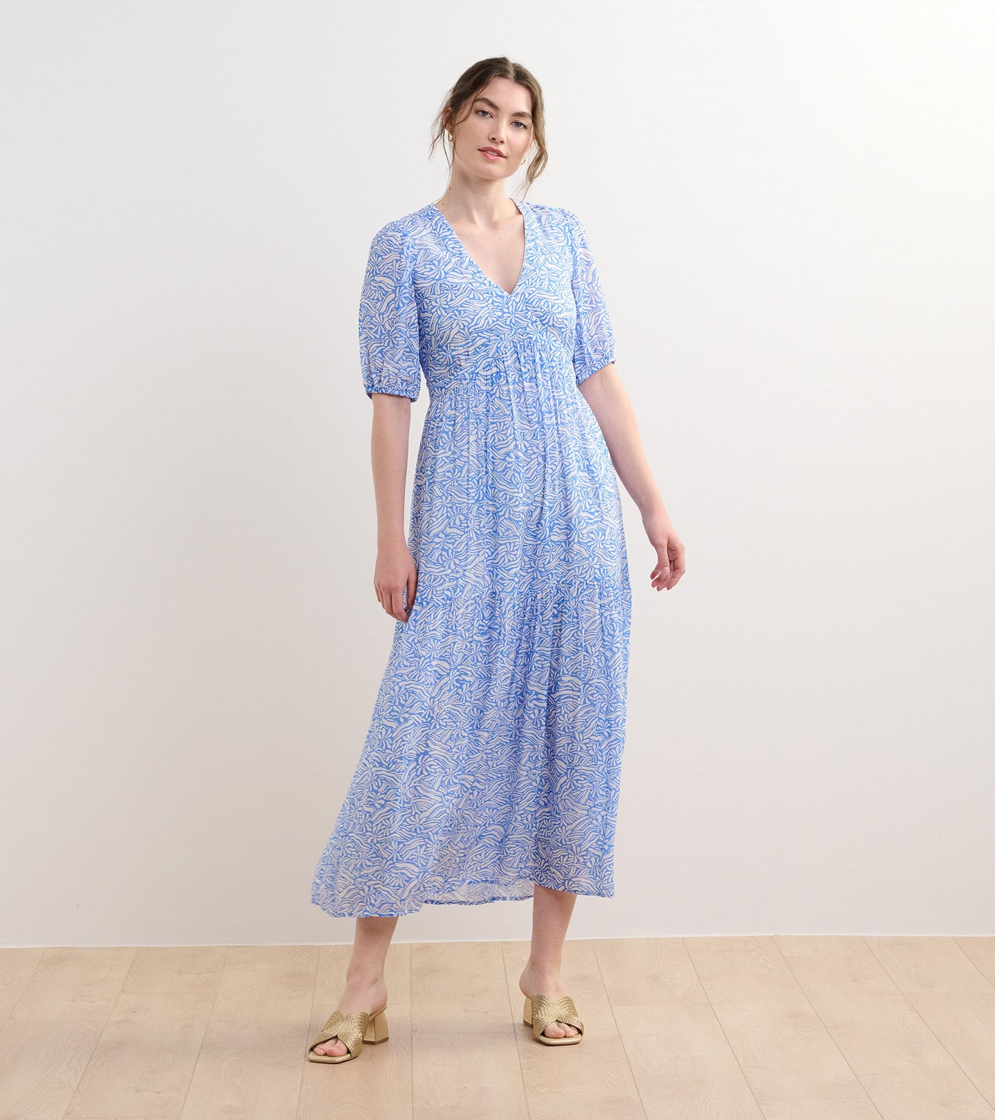 Light blue maxi dress with a floral pattern, short puff sleeves, and a V-neckline, styled with gold heeled sandals.