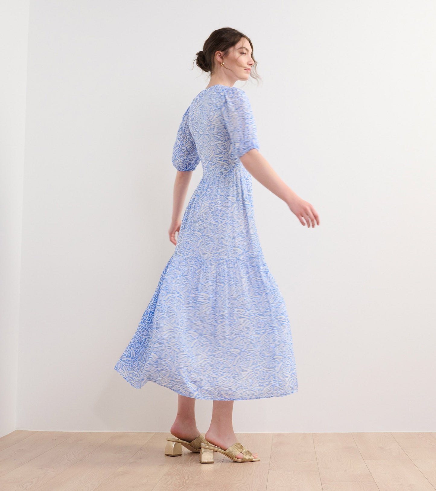 Light blue dress with a groovy floral pattern, featuring puff sleeves and a flowing skirt, worn with gold heeled sandals.