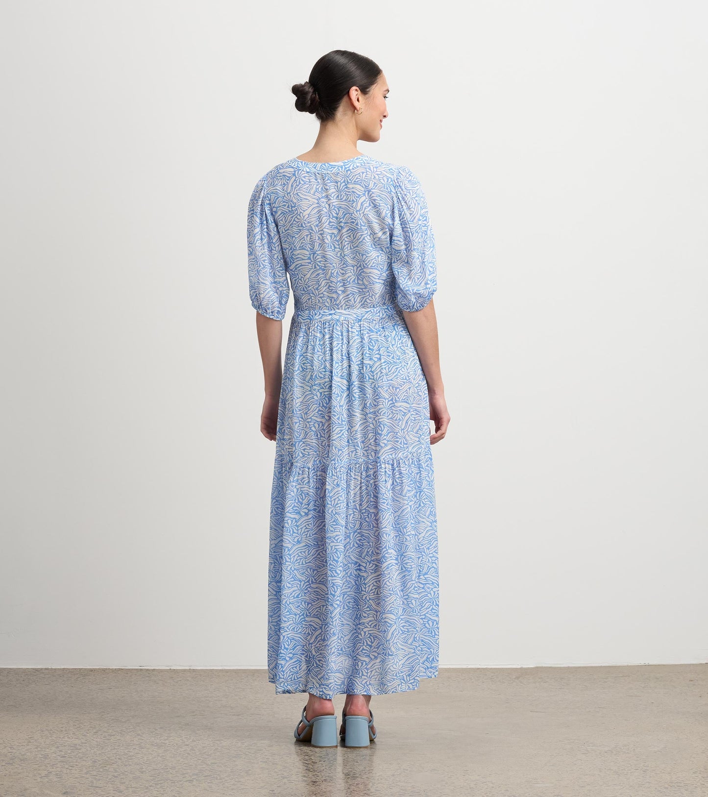 Long blue dress with a groovy floral pattern, featuring puff sleeves and a tiered skirt, shown from the back.