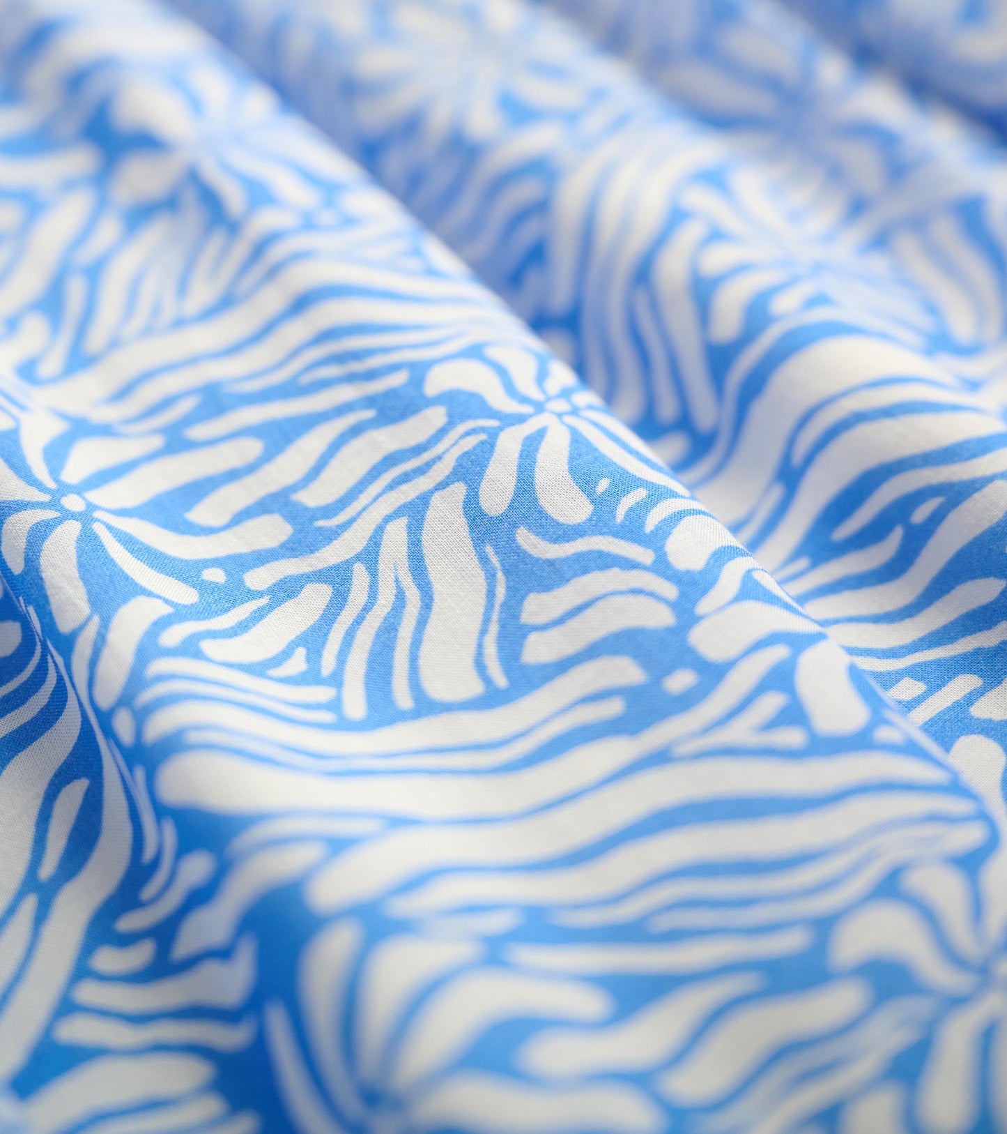 Blue fabric featuring a groovy floral pattern in white, showcasing a soft and flowing texture.