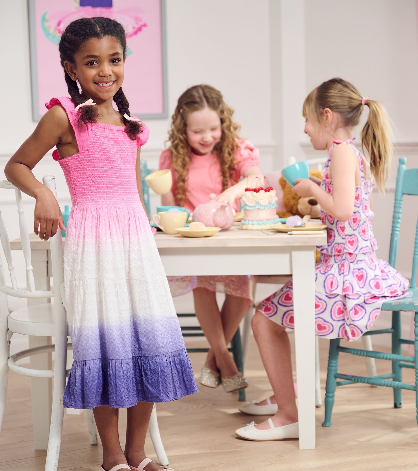 Smocked angel dress with pink to purple ombre, featuring ruffled straps, worn by a girl at a tea party with friends.