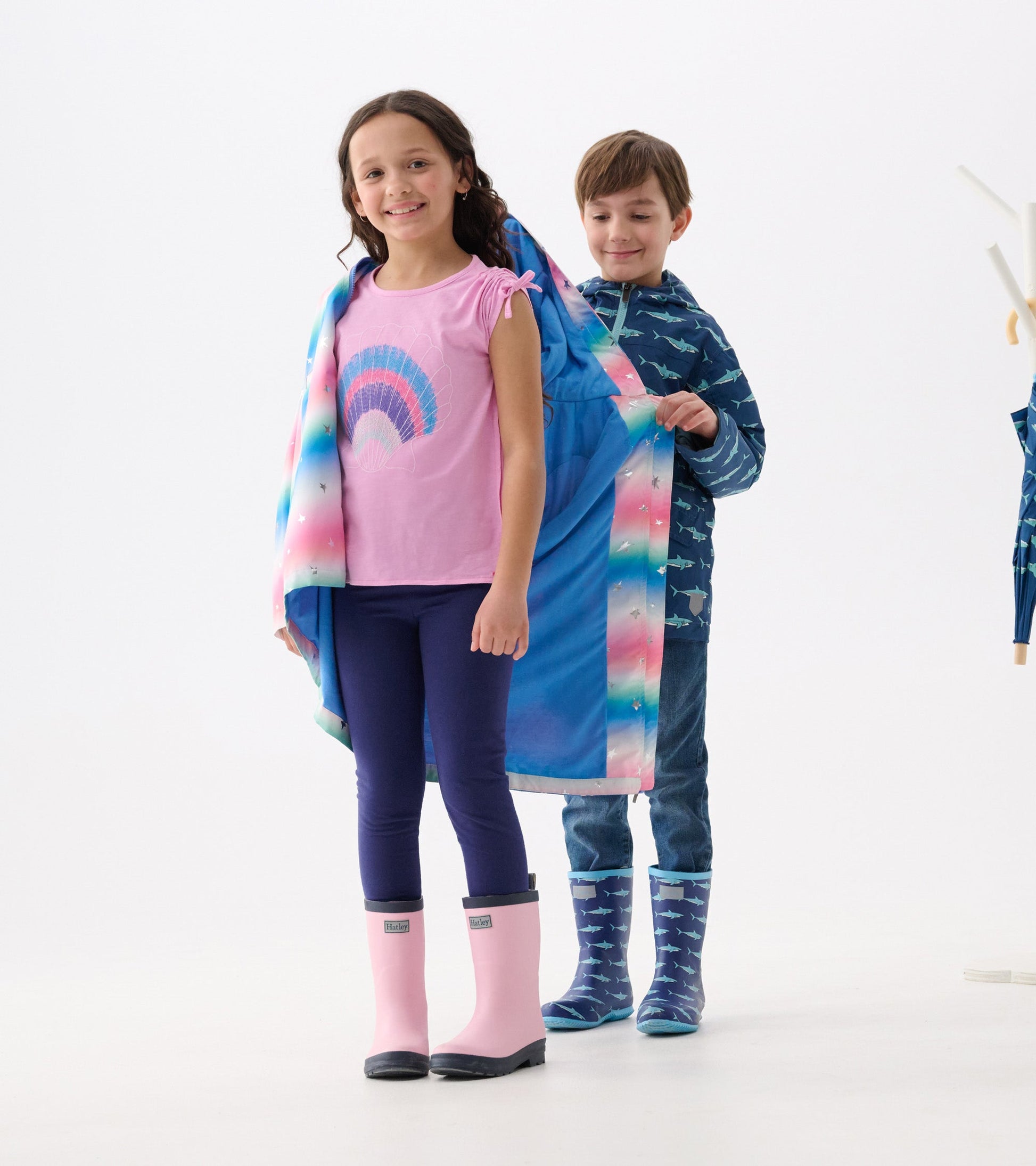 A girl in a pink top and leggings wears a colorful glitter star A-line swing jacket, while a boy stands behind her.