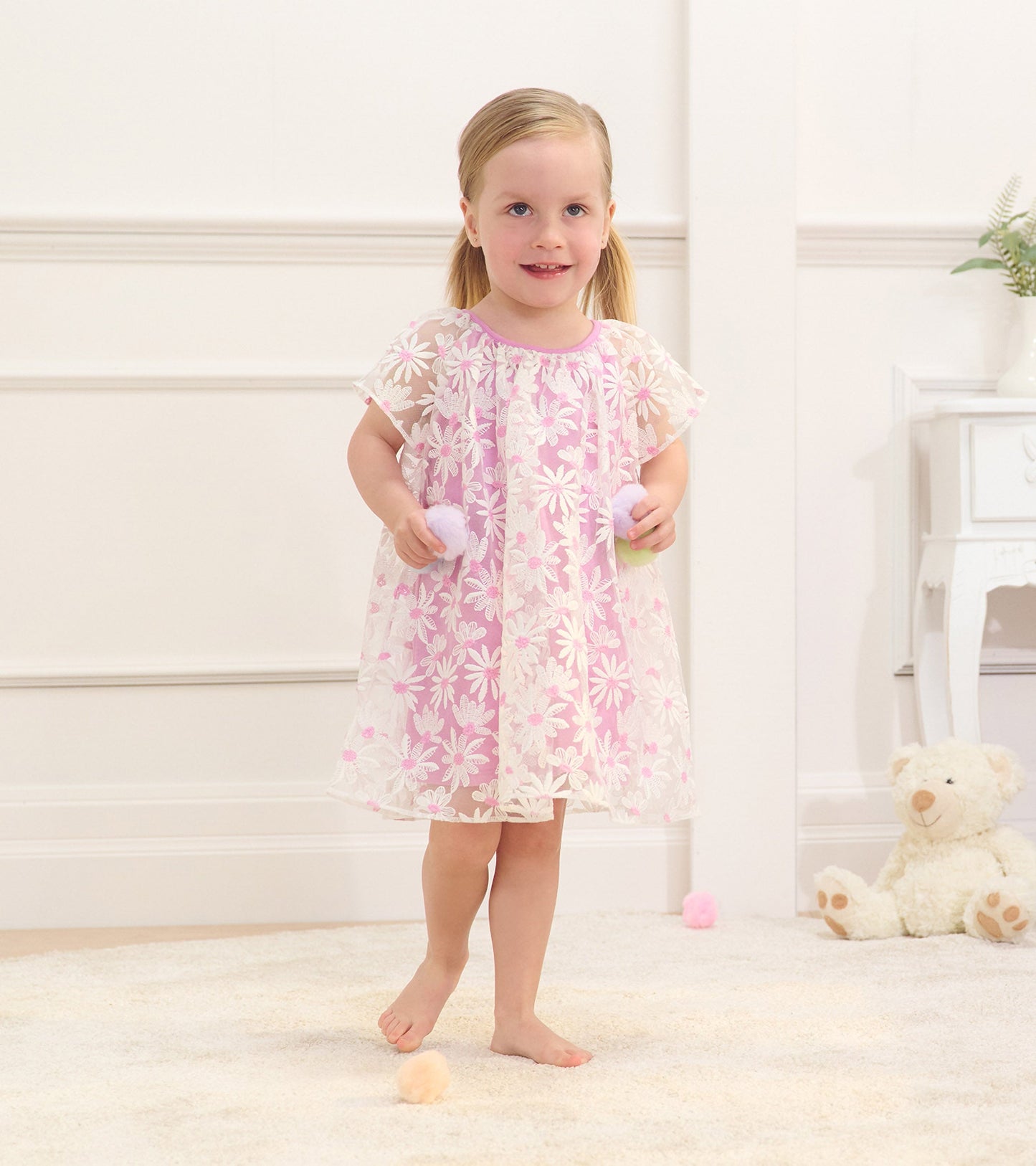 Lilac tulle dress with white daisy pattern, short sleeves, and a loose fit, worn by a girl holding colorful pom-poms.