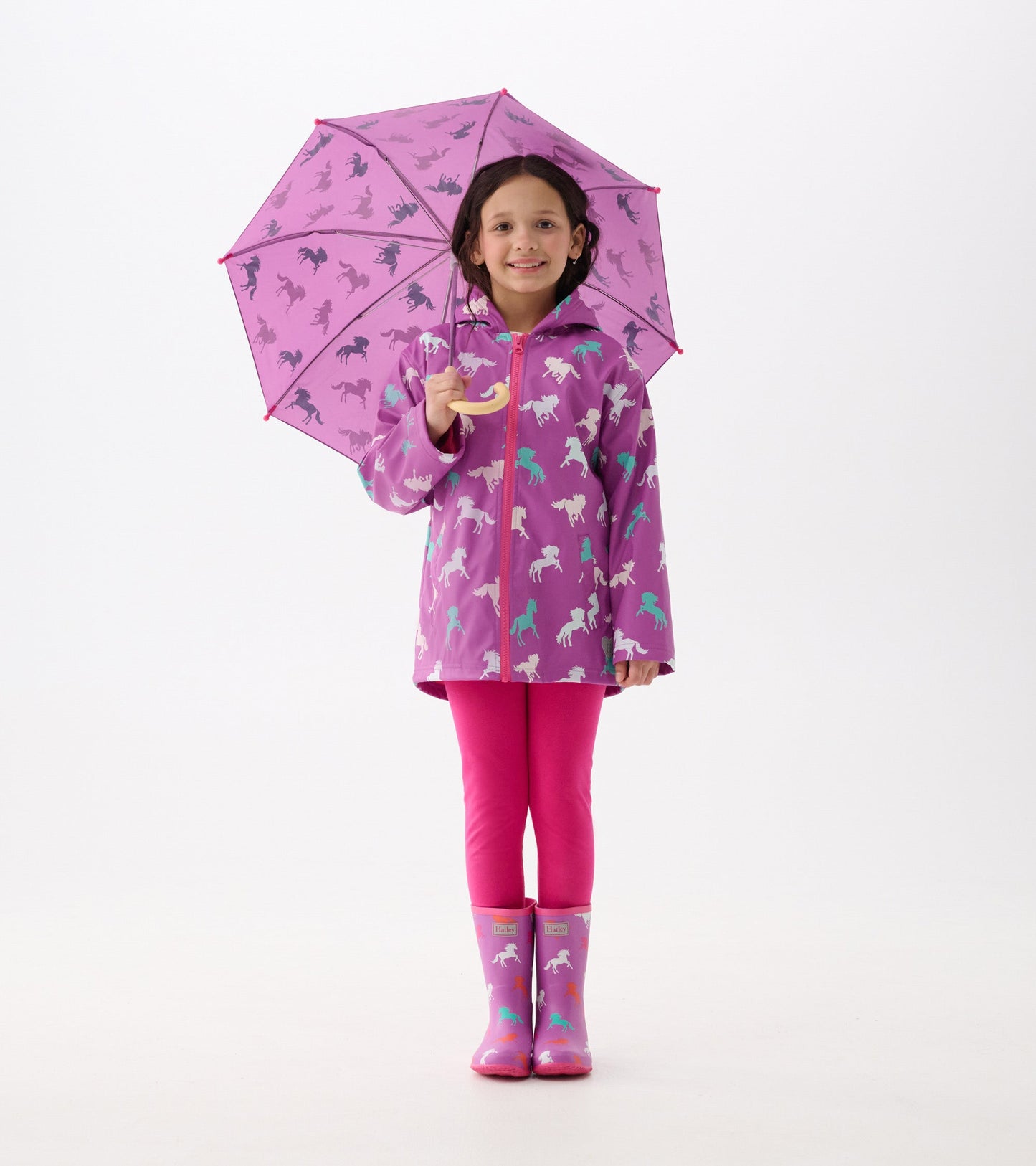 Purple rain boots with horse patterns, paired with a matching raincoat and pink leggings, held by a smiling girl.