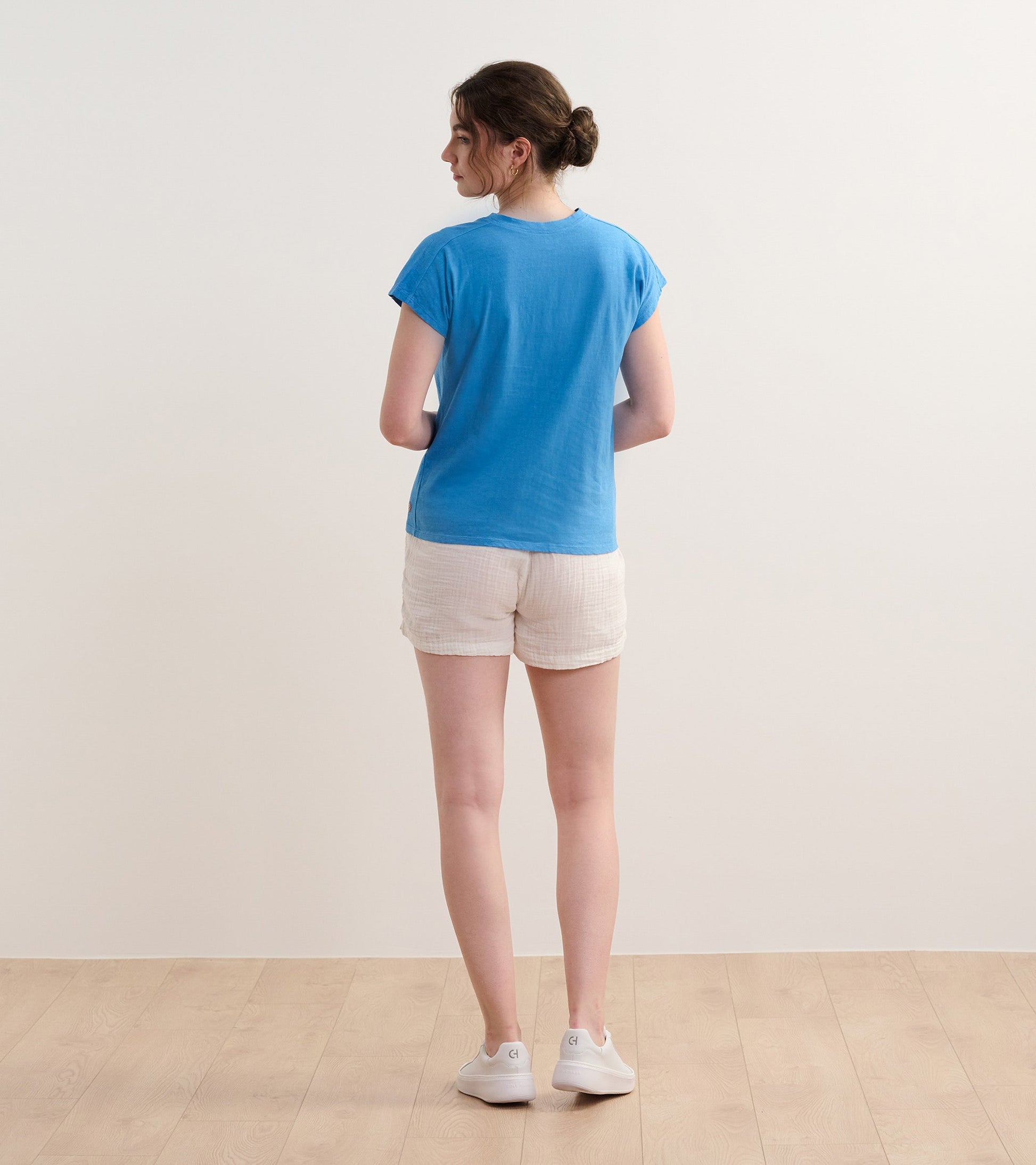 Back view of a slouchy blue tee with short sleeves, paired with light shorts and white sneakers.