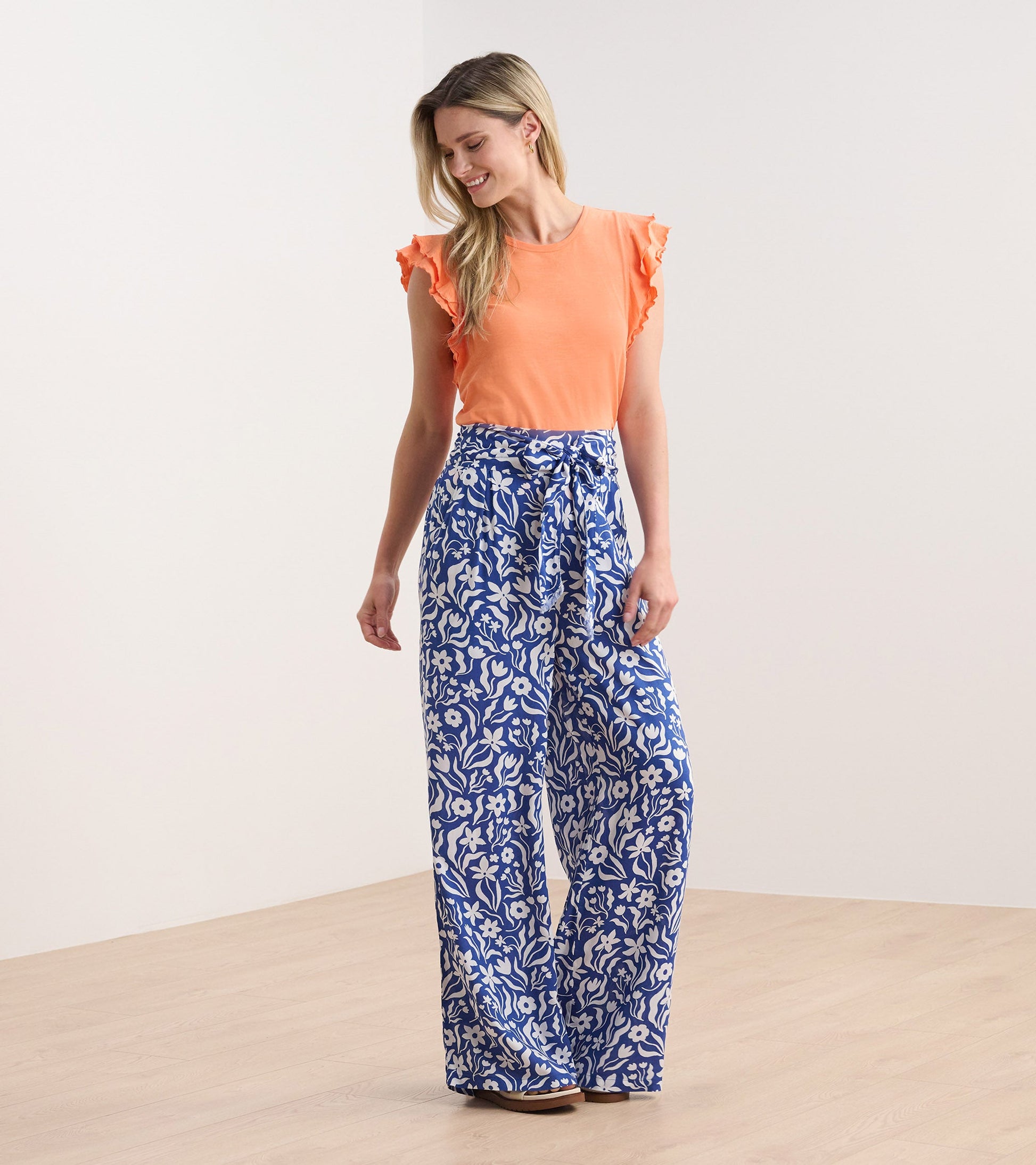 Melon-colored tank top with layered ruffle sleeves, paired with wide-leg floral patterned pants.