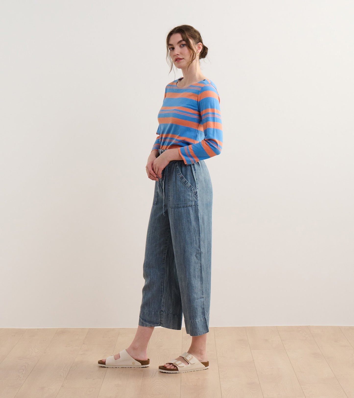 Striped long-sleeve top in blue and melon, paired with light denim wide-leg pants and sandals.