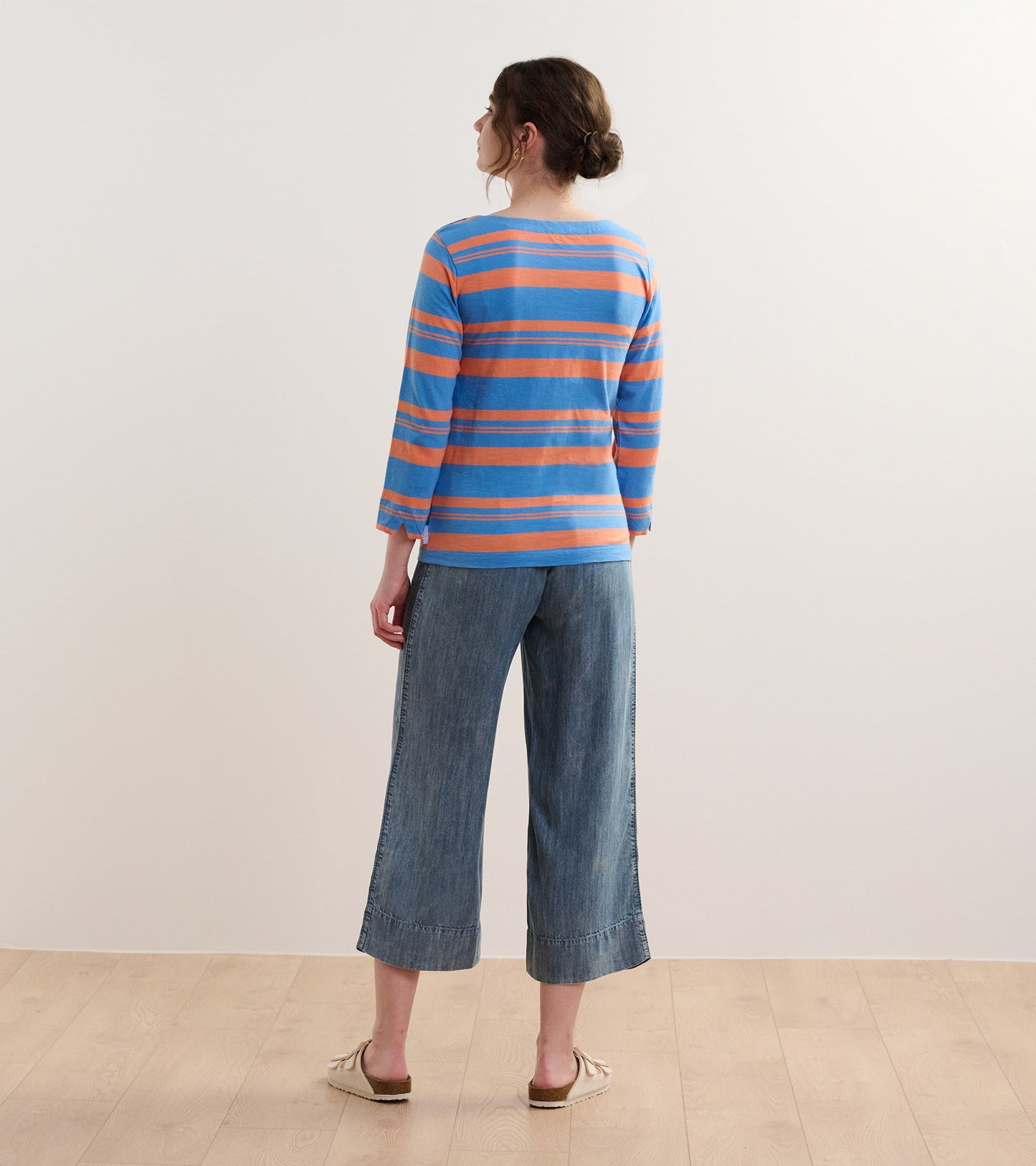Back view of a long-sleeve striped top in blue and melon, paired with wide-leg denim pants.