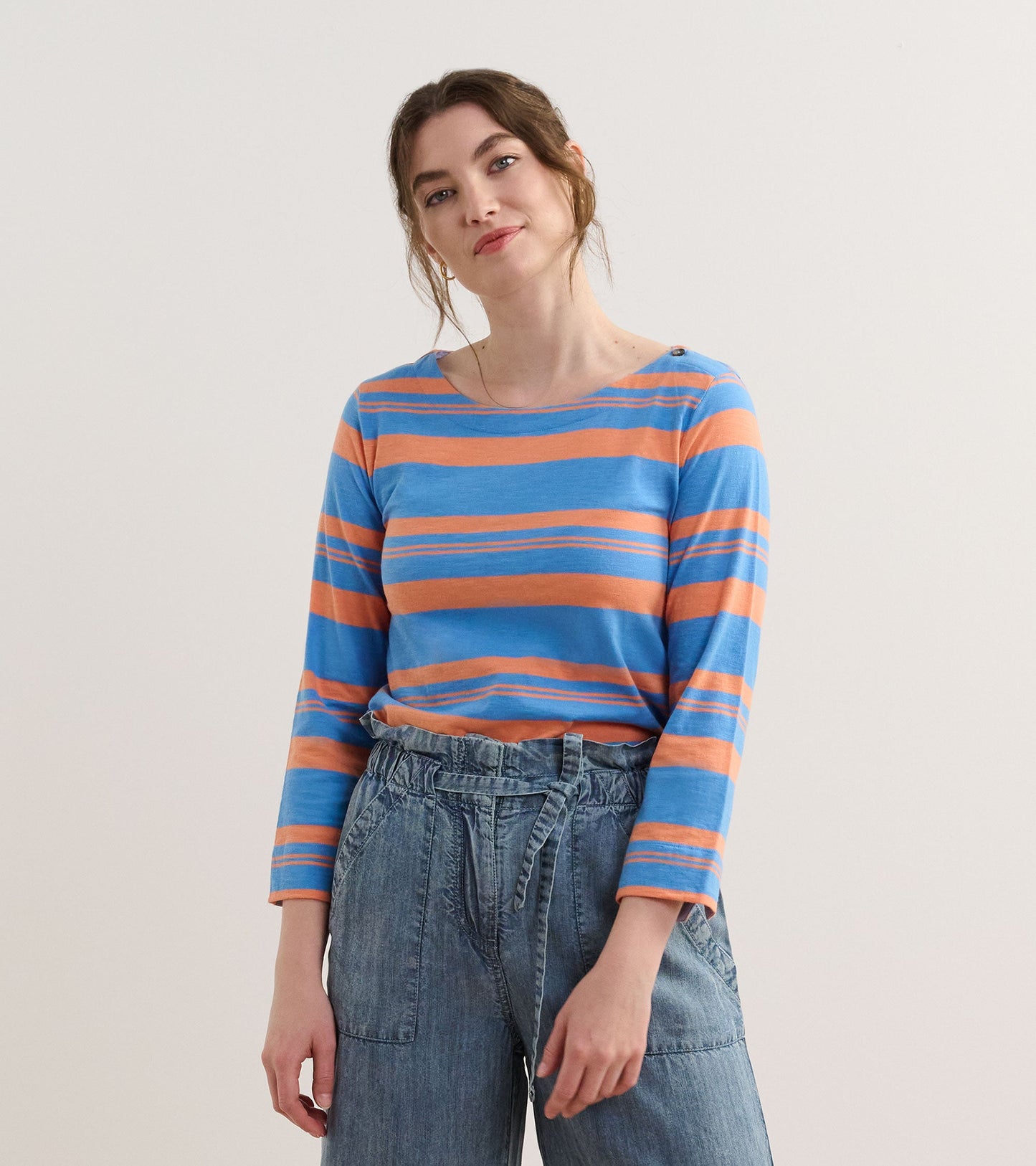 Long-sleeve top featuring blue and melon stripes, round neckline, and relaxed fit, paired with denim pants.