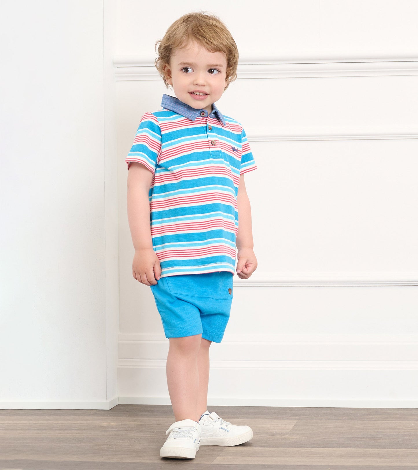 Striped polo tee in blue, red, and white, featuring a collared neckline, paired with blue shorts.