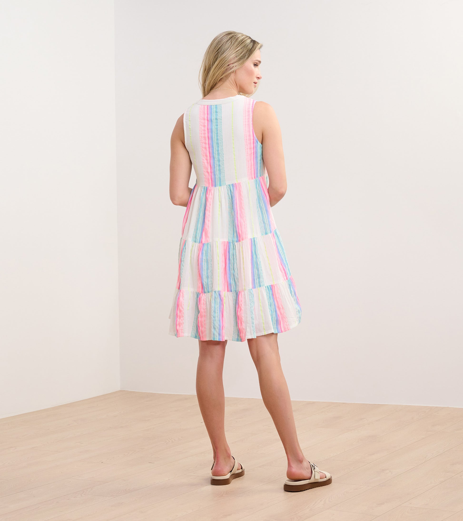 Back view of a sleeveless dress featuring neon bright stripes in pink, blue, and green with a tiered skirt.