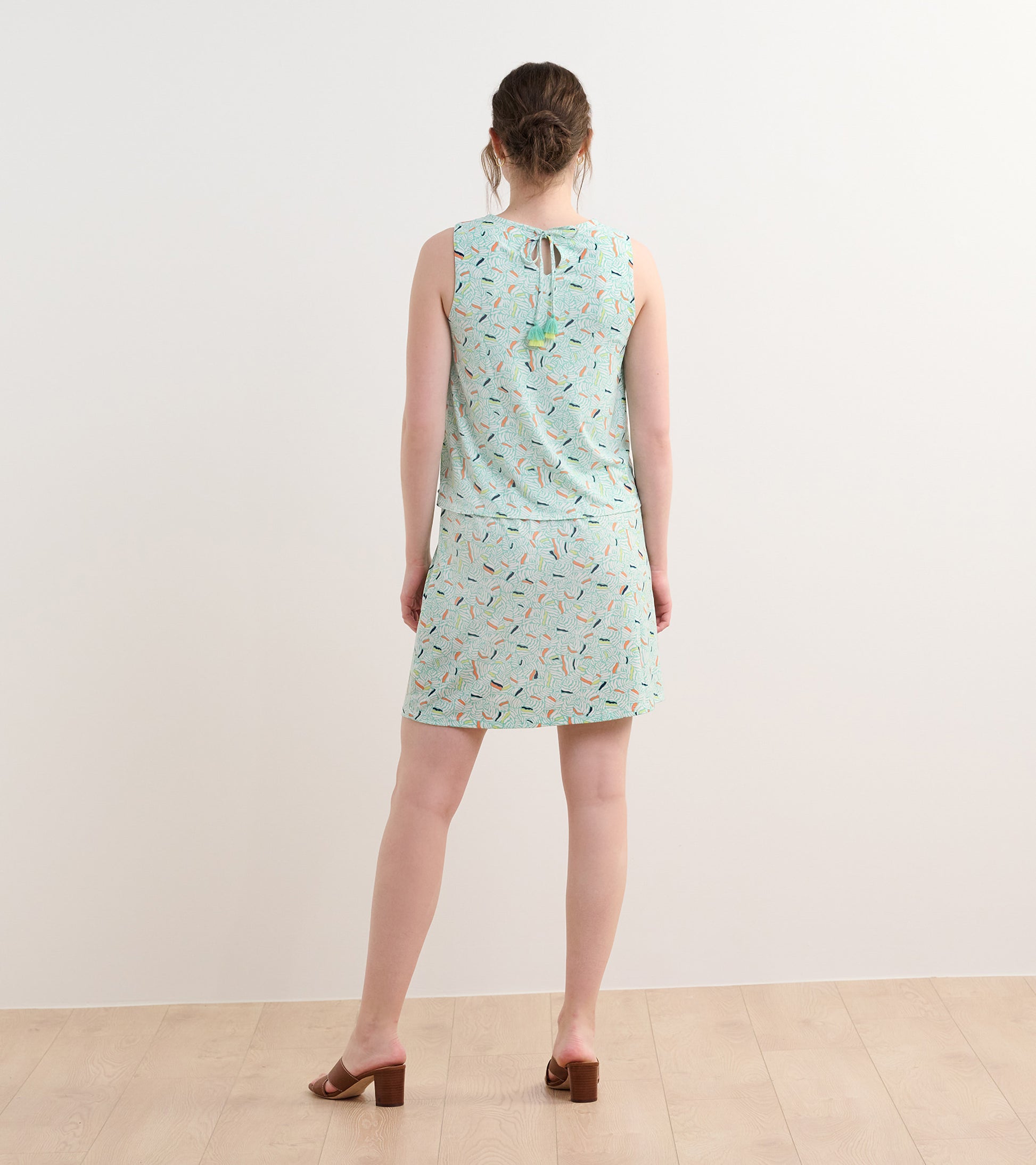 Sleeveless dress in light green with a leaf pattern, featuring a tie at the back and a flared skirt.