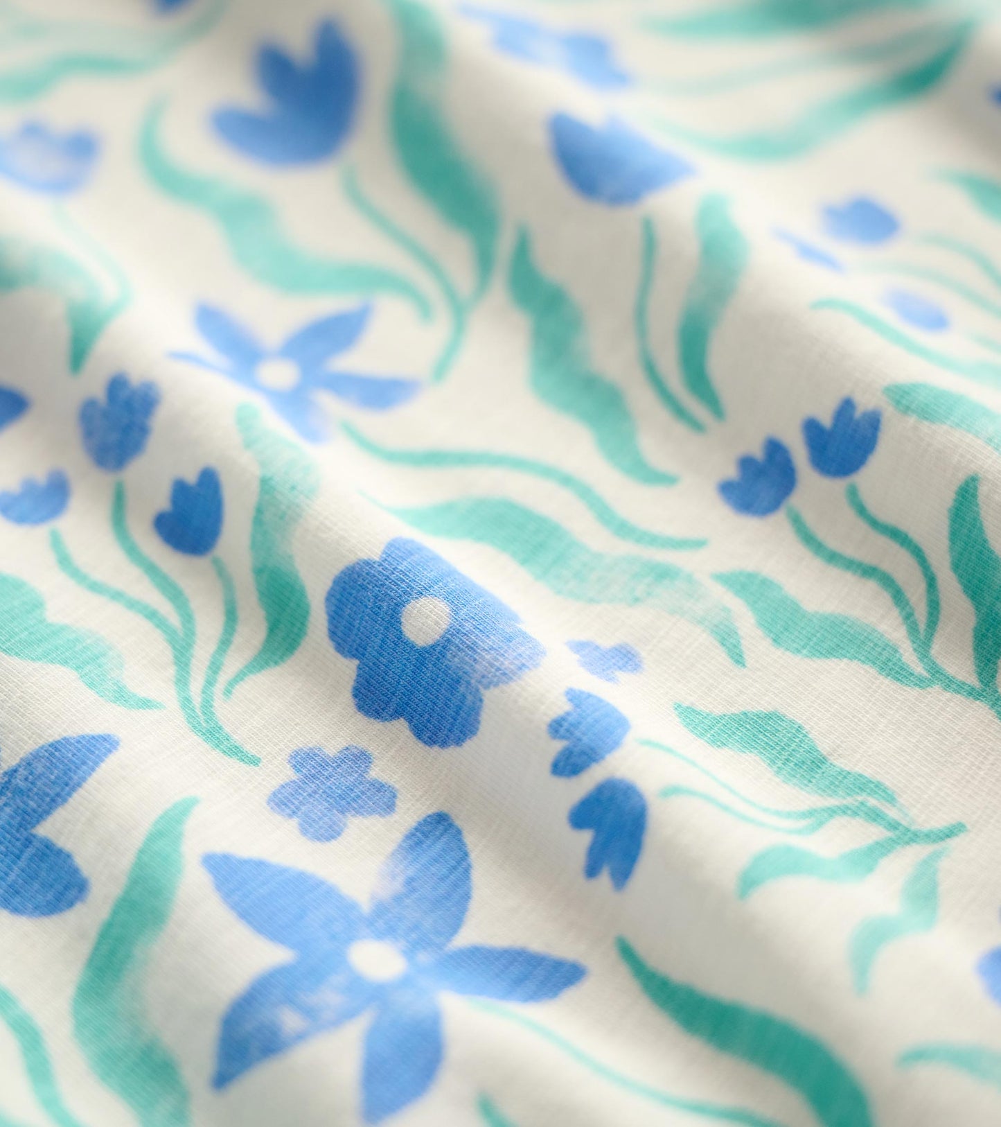 White fabric featuring a floral pattern in blue and teal hues, with various flower shapes and green leaves.