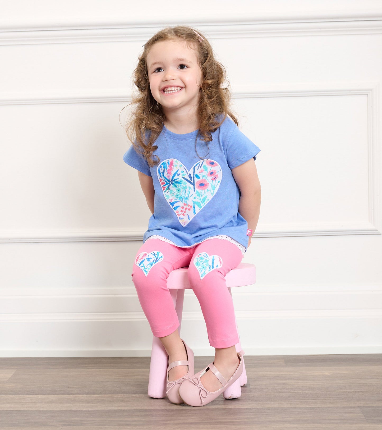 Light blue t-shirt with a floral heart design, paired with pink leggings featuring heart patches, worn by a smiling girl.