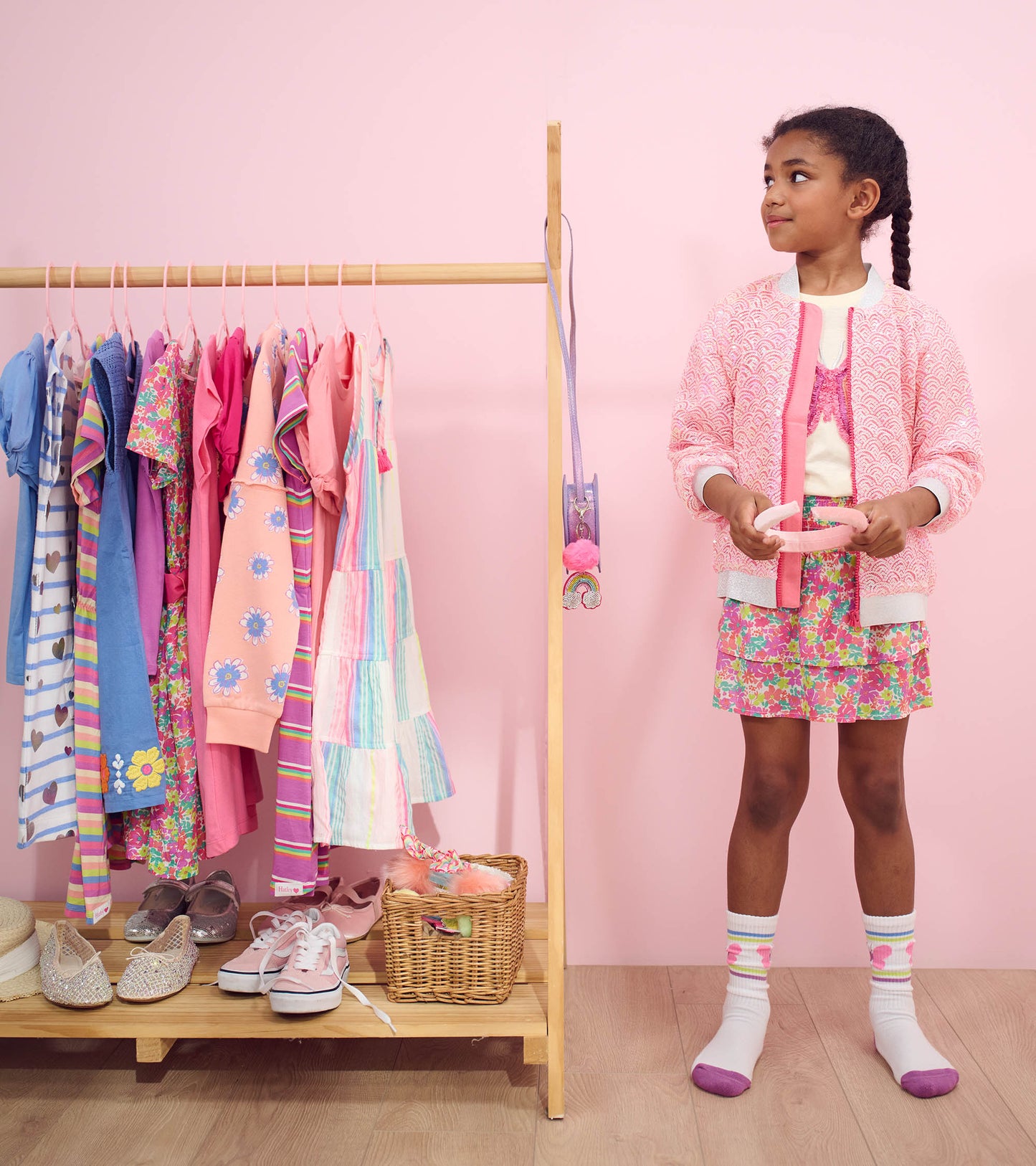 Pink sequined bomber jacket with mermaid scale pattern, worn over a floral skirt, displayed in a colorful children's wardrob…