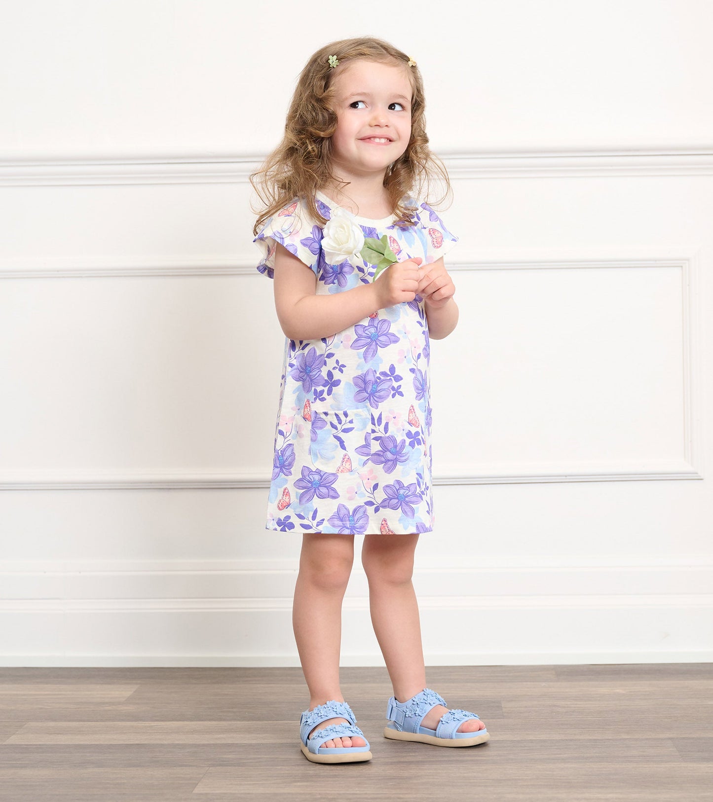 Light purple dress with painted magnolia flowers, short ruffled sleeves, worn by a smiling girl with curly hair.