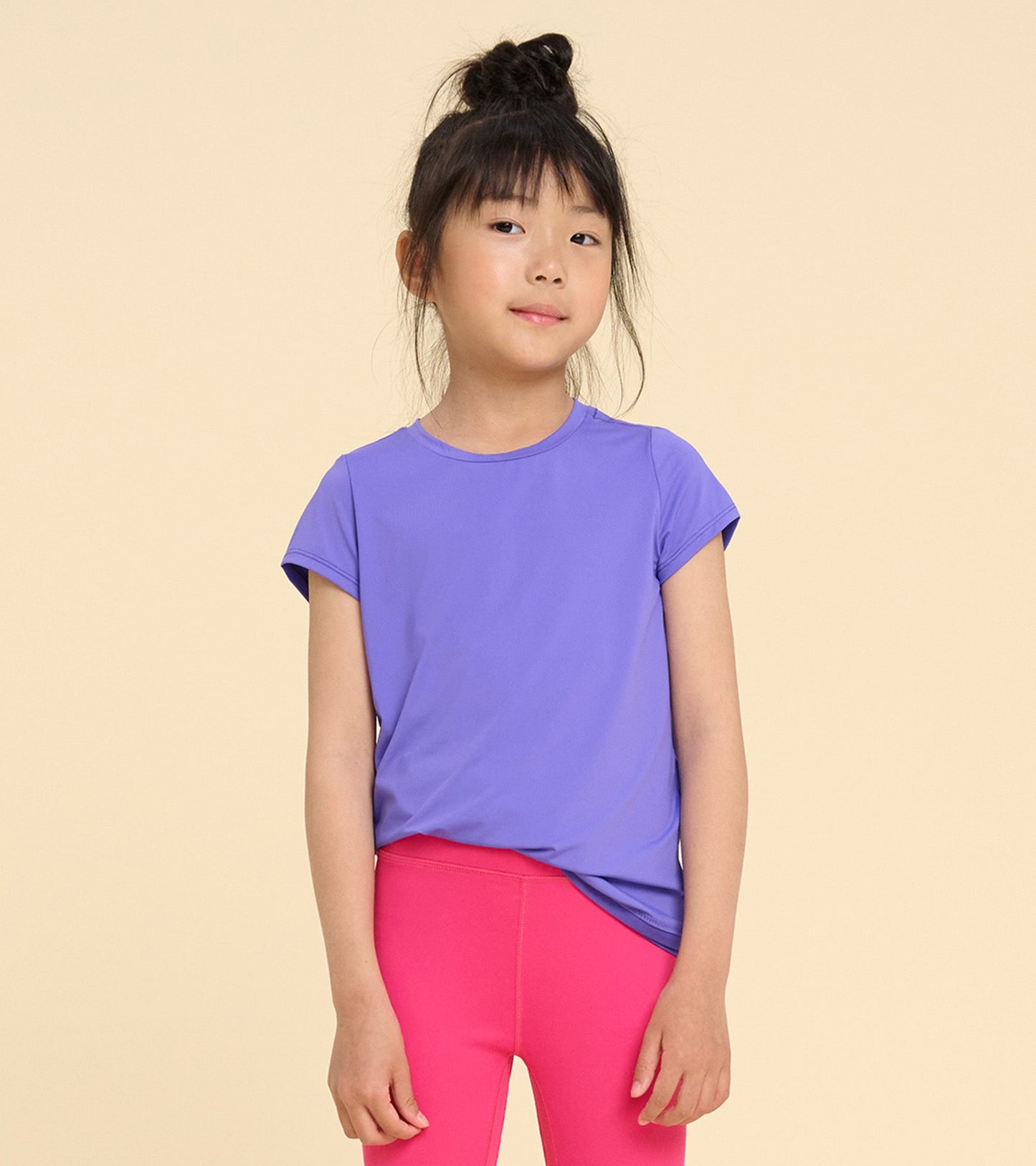 Purple short-sleeve t-shirt with a smooth texture, paired with pink leggings, worn by a girl against a neutral background.
